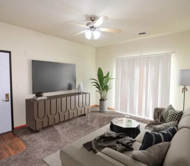 Chic and inviting living room featuring a stylish sofa, modern entertainment center with a large TV, and lush greenery, all bathed in natural light from expansive windows.