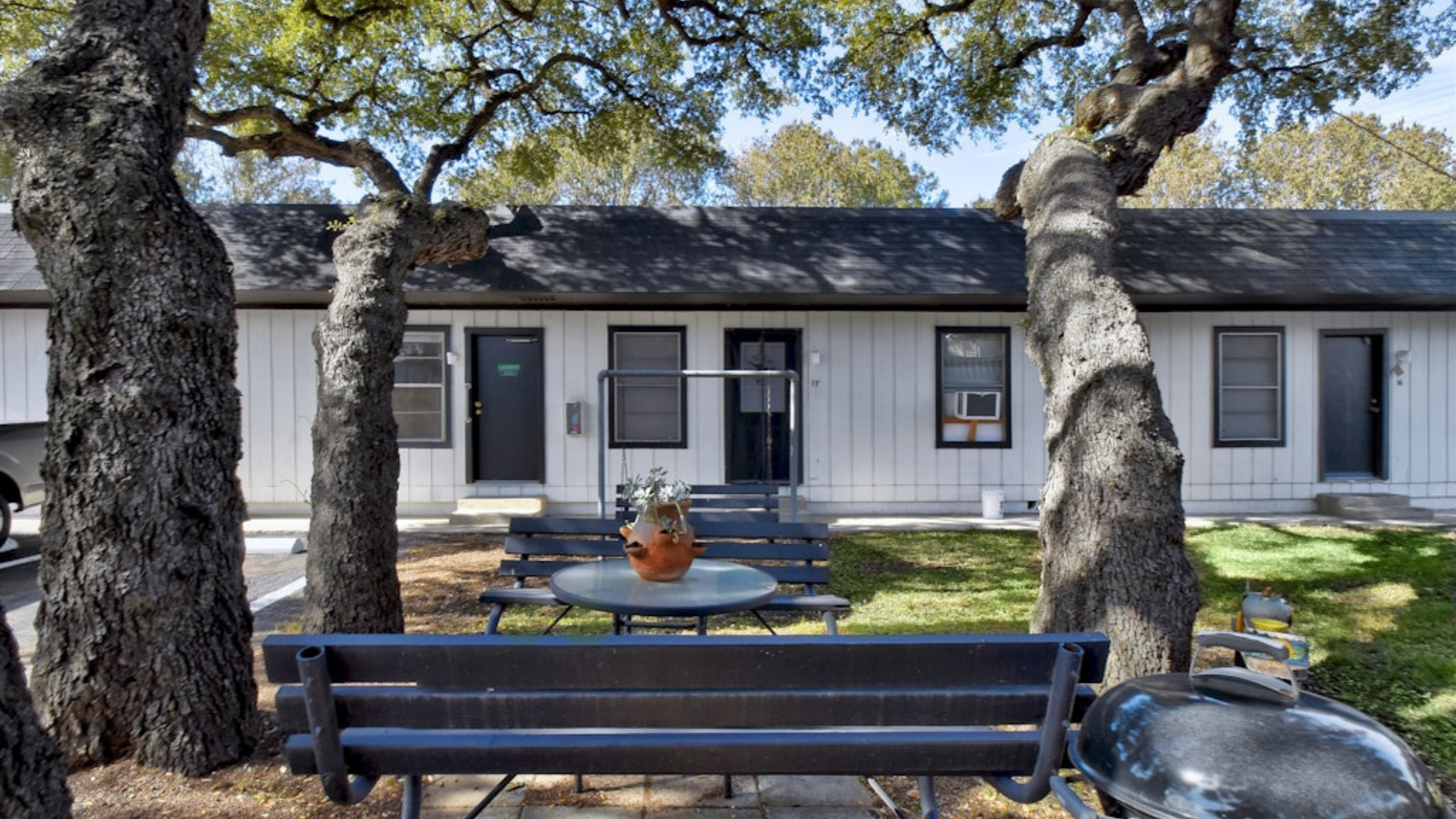Charming outdoor view of a quaint apartment complex with a cozy seating area shaded by mature trees.
