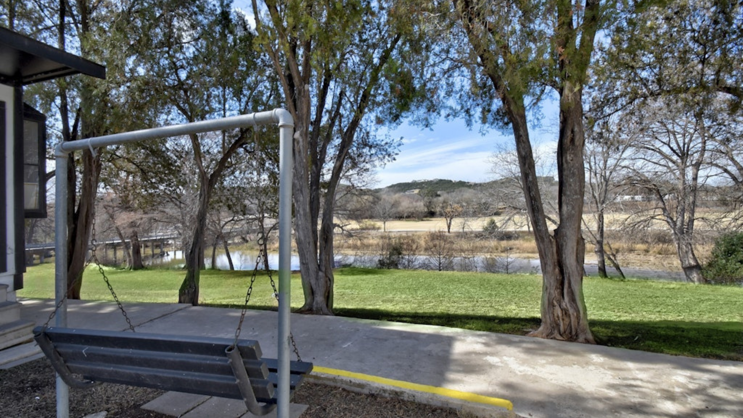 Charming outdoor view with a cozy swing overlooking serene trees, lush greenery, and a tranquil river beyond.