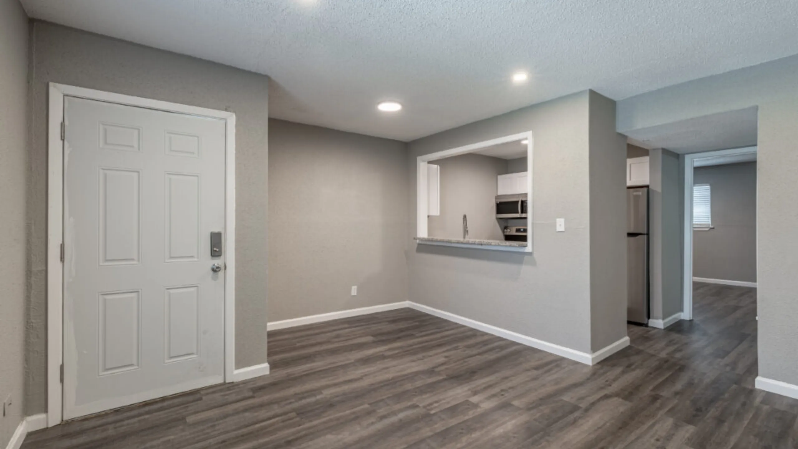 Charming apartment with sleek modern flooring, open entryway, and a peek-through kitchen window for seamless living.