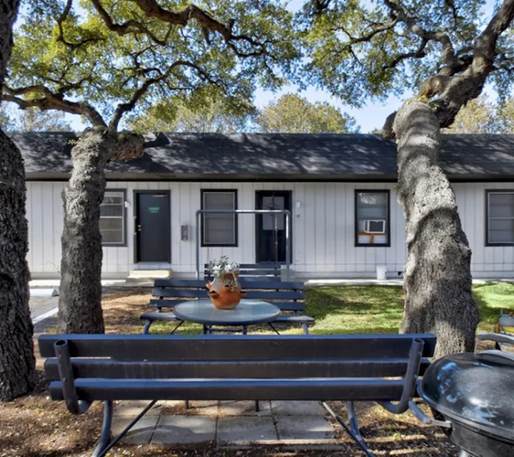 Charming outdoor space featuring cozy benches under shady trees, perfect for relaxation with a scenic view of a quaint cottage-like apartment entrance.