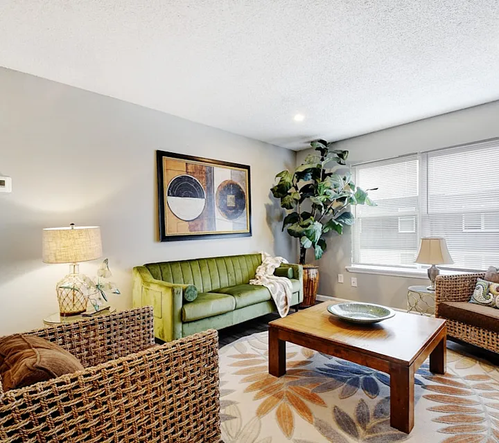 Inviting modern living room featuring a vibrant green sofa, woven armchairs, and a stylish wooden coffee table. Large windows enhance the space with natural light.