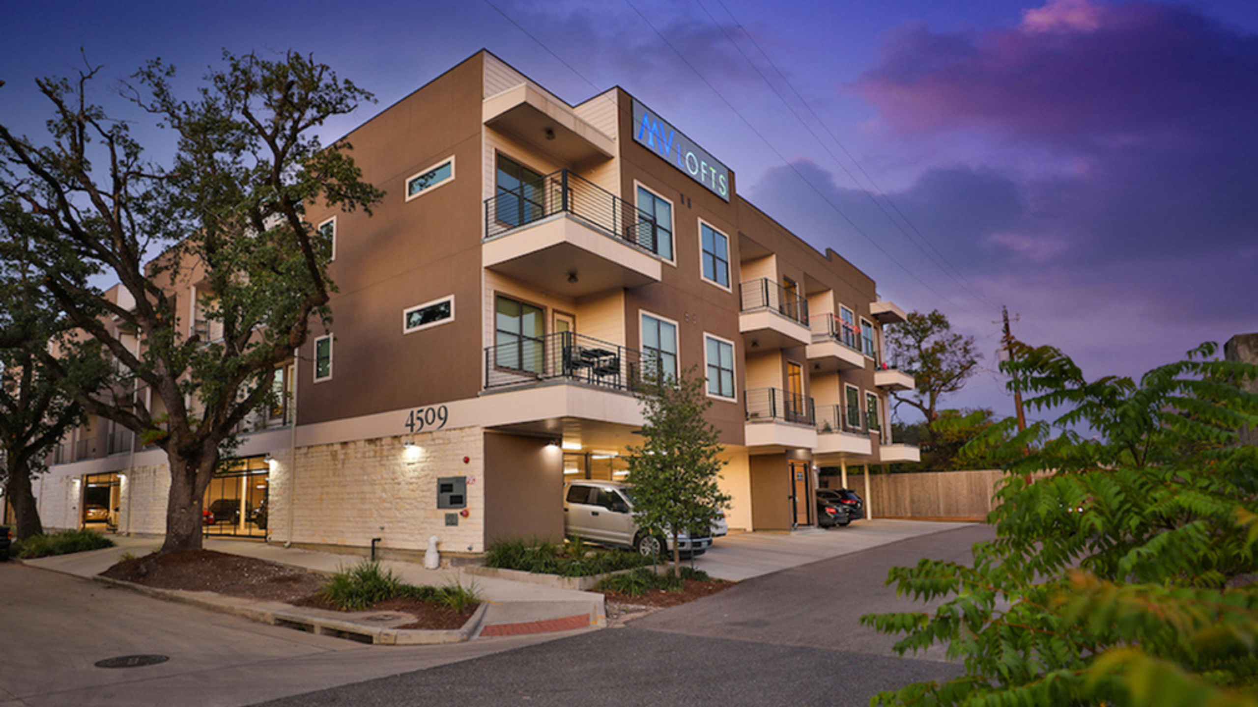 Elegant modern apartment building at sunset with spacious balconies, surrounded by lush greenery and a tranquil ambiance.