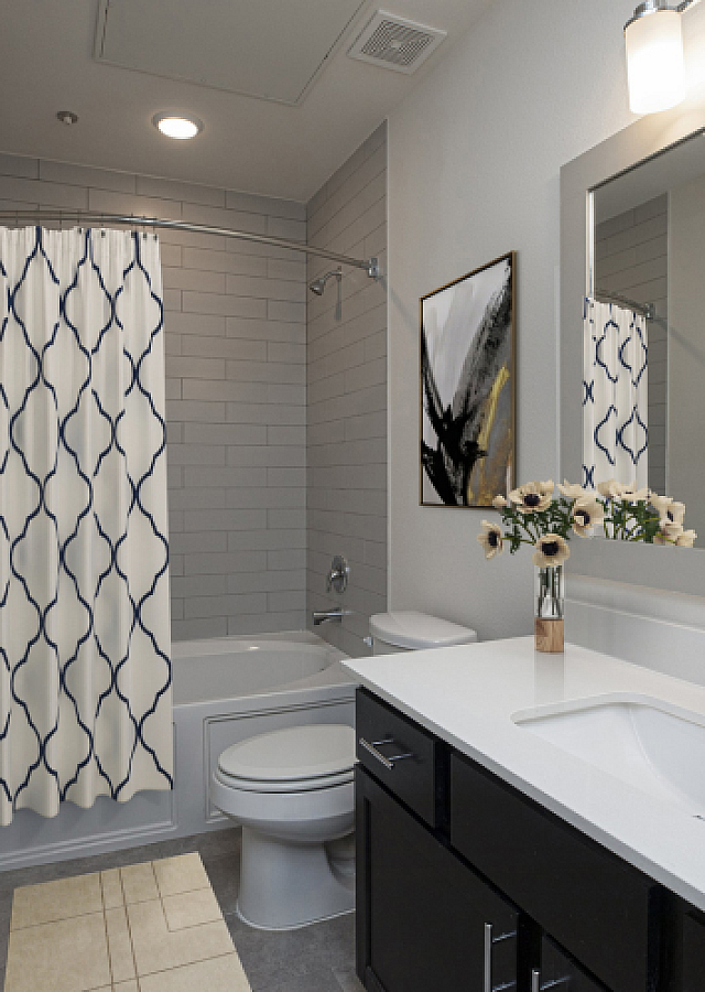 Modern bathroom with elegant gray tile, stylish shower curtain, and contemporary vanity, featuring chic lighting and decor accents.