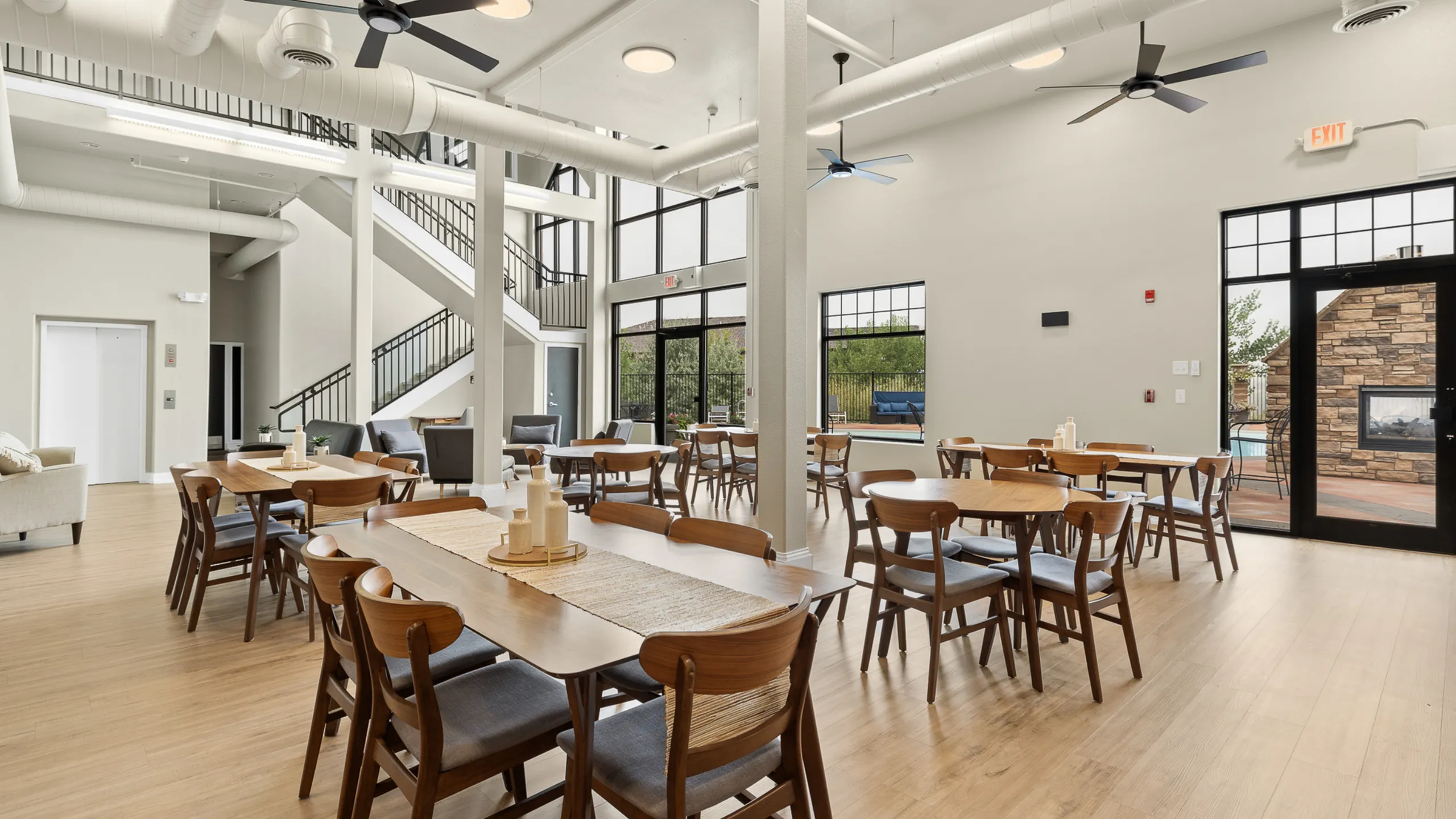 Chic community area with modern dining tables, elegant wooden flooring, and abundant natural light from large windows.