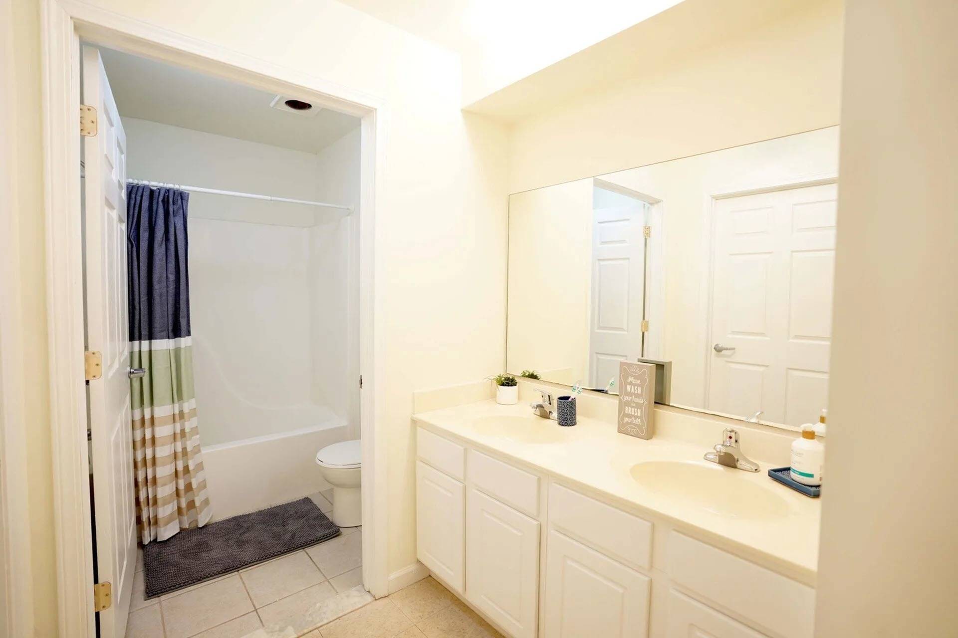 Dog-Friendly Apartments In Mansfield, PA - Commons At Mansfield - Bathroom With White Cabinets, Large Vanity Mirror, Dual Sinks, And A Shower, Tub Combo.