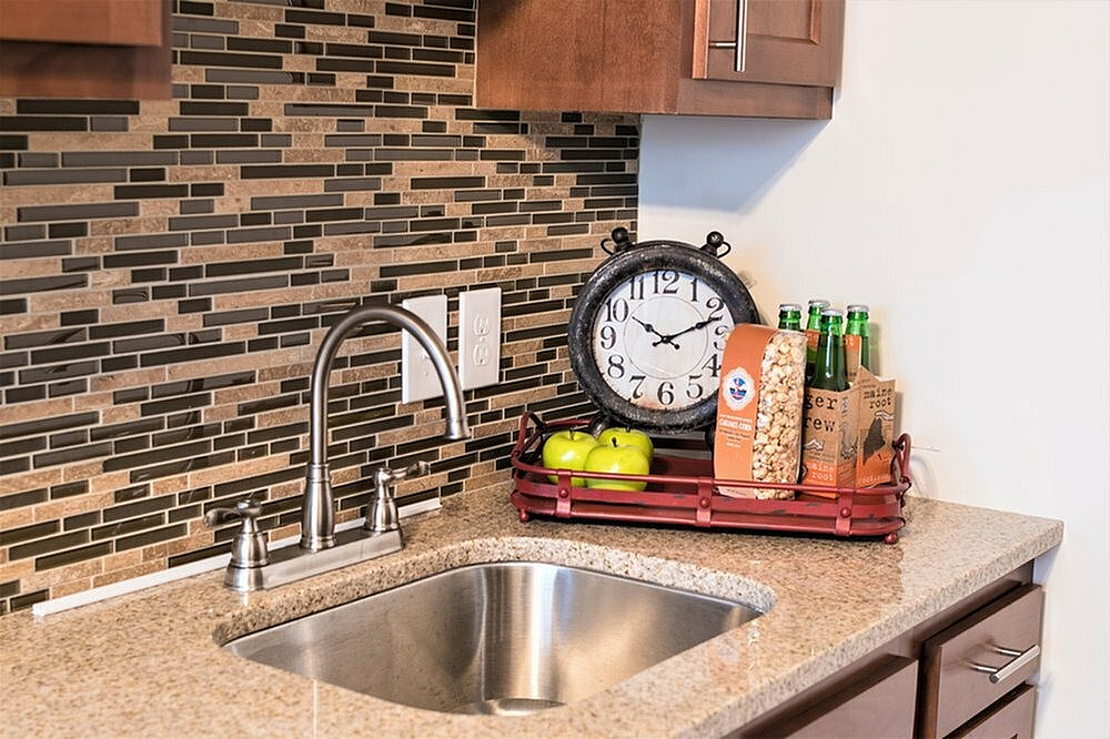 Sophisticated kitchen counter with polished granite surface, modern faucet, and decorative elements including a vintage clock and a snack display.