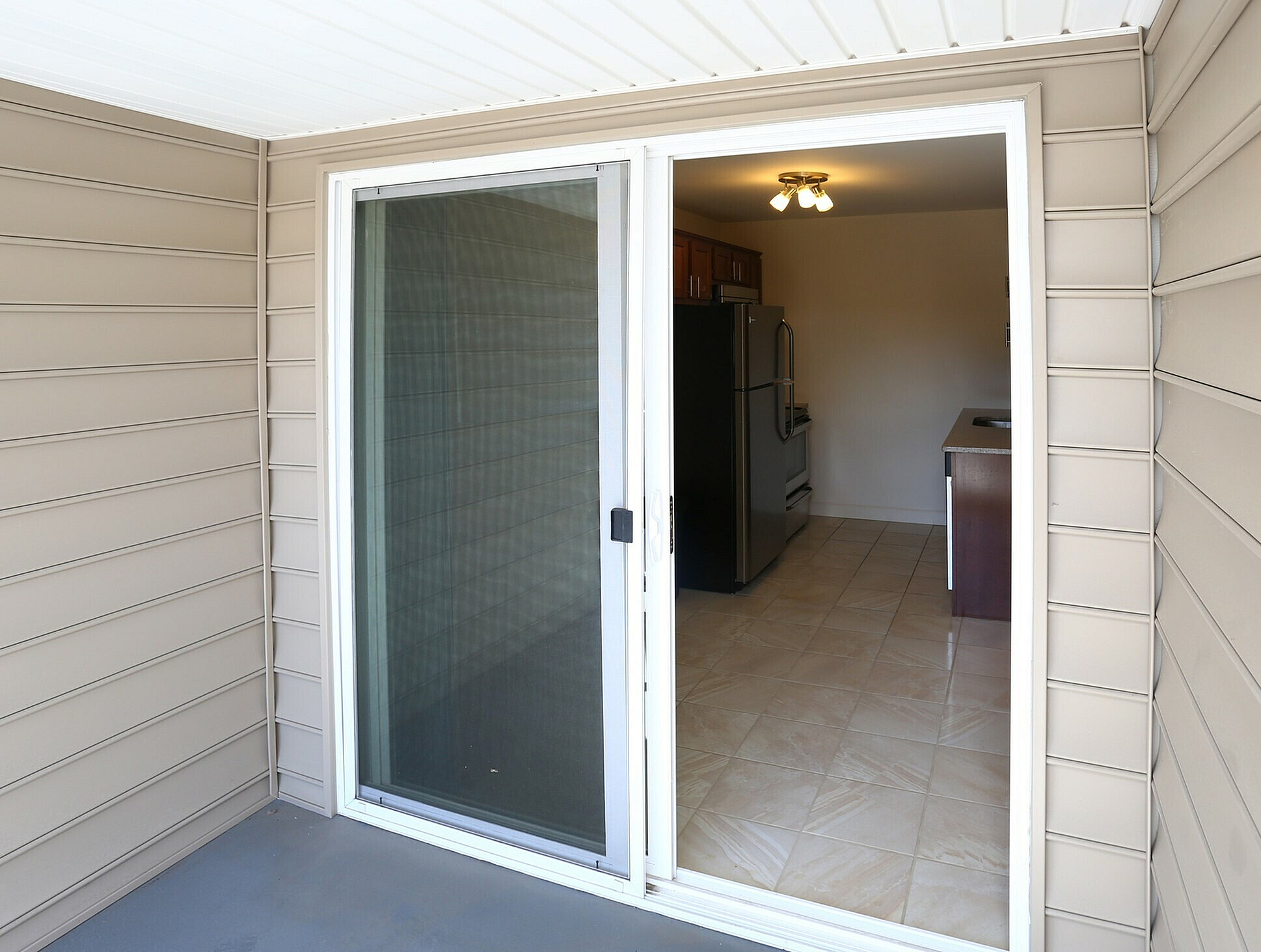 View of a modern kitchen through a sliding glass door from a patio area with beige siding.