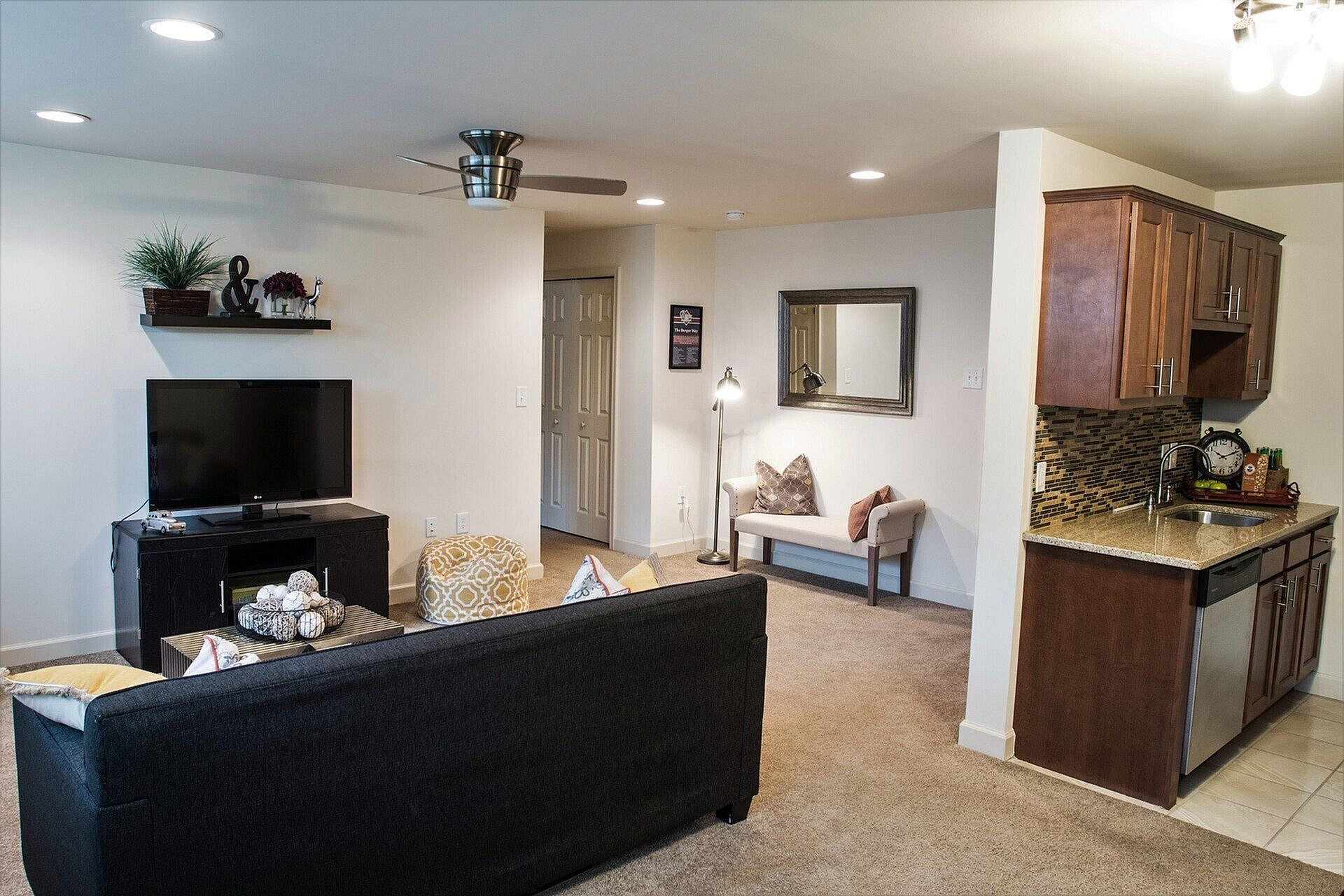 Inviting open-concept living room with cozy seating, modern TV setup, and elegant kitchen corner, perfect for relaxation and social gatherings.