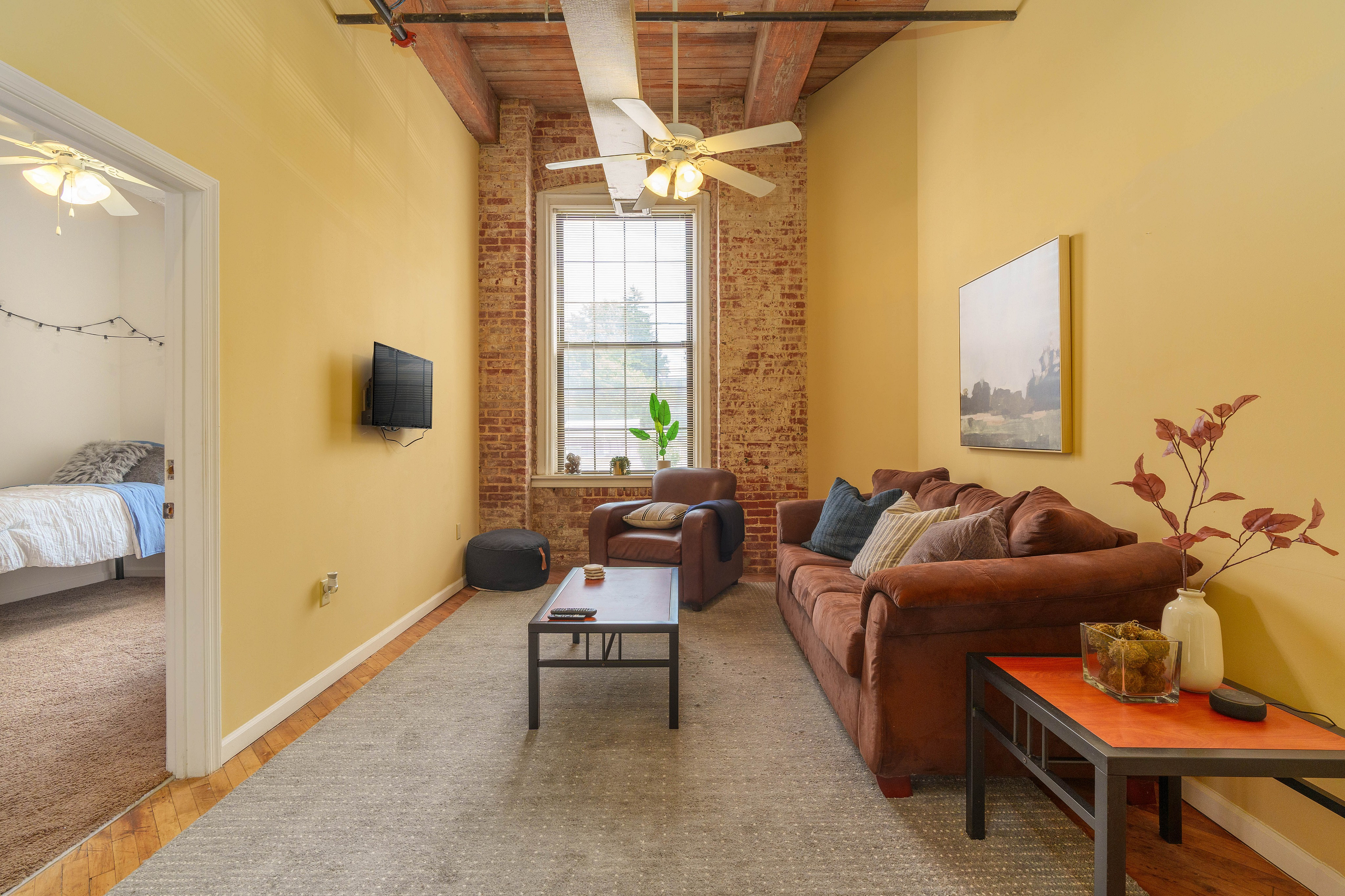 Charming living room with exposed brick walls, cozy brown sofas, and a large window for abundant natural light.