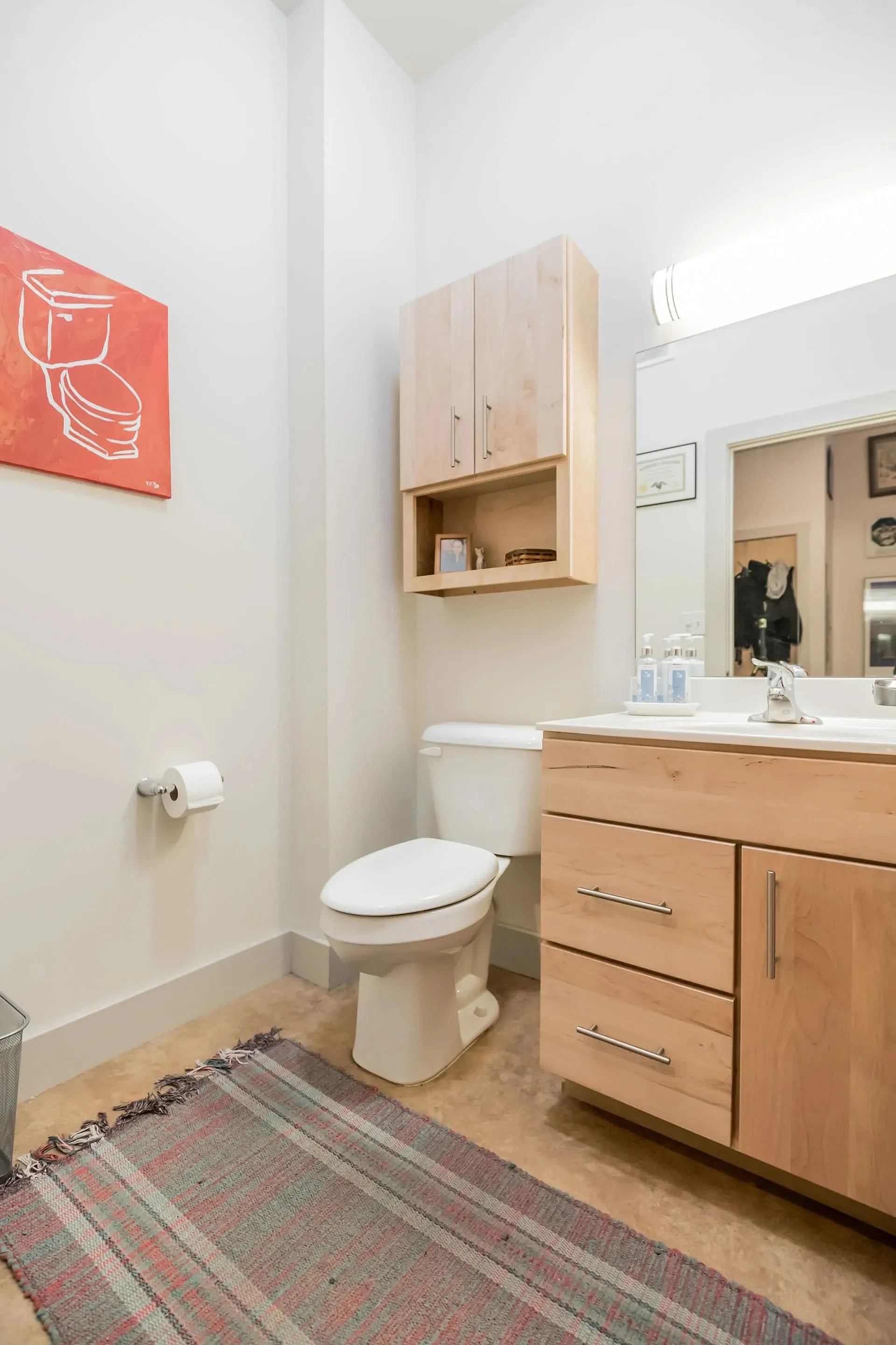 Modern bathroom with sleek wooden cabinetry, stylish wall art, and cozy rug for a welcoming touch.