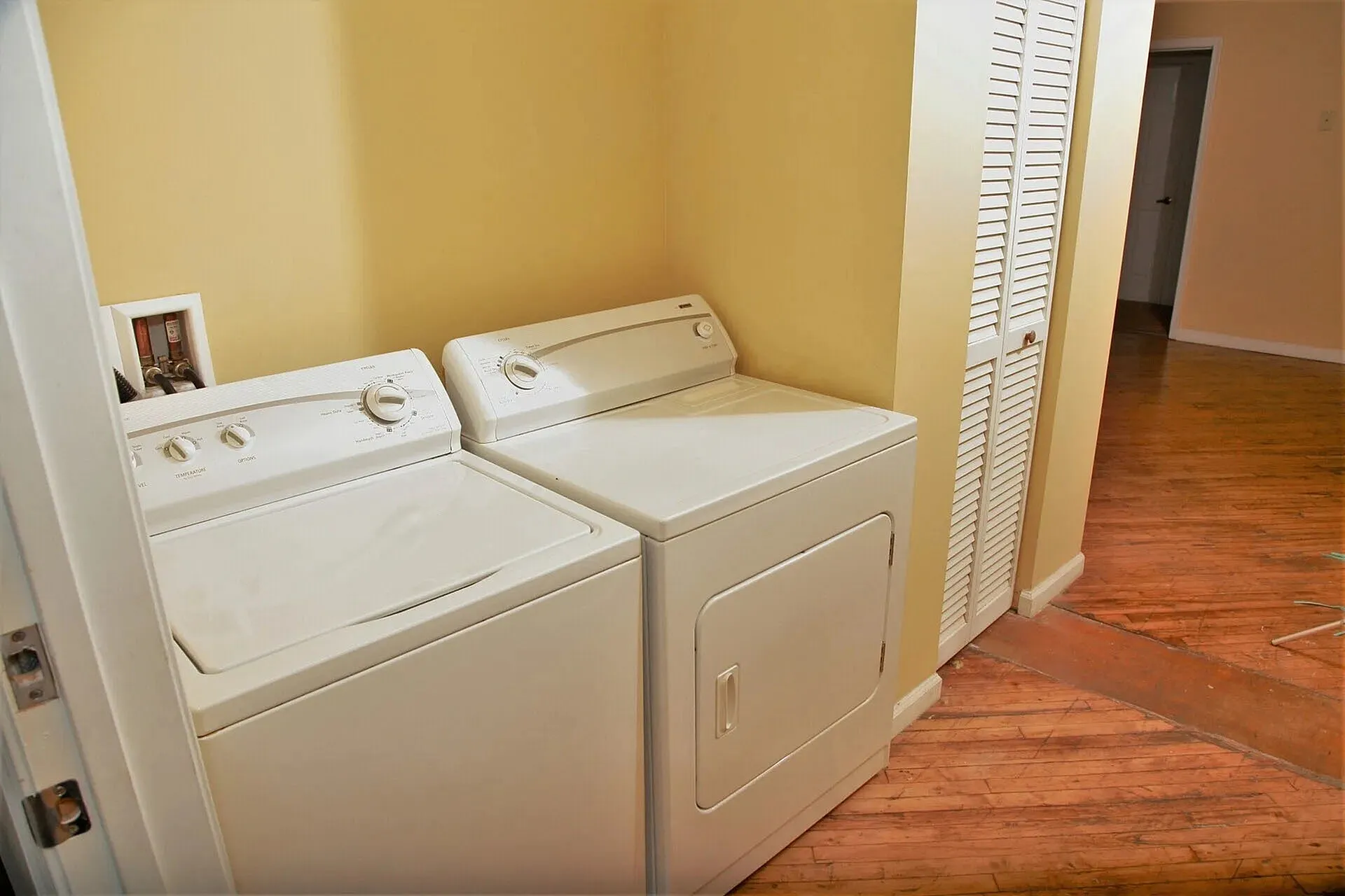 Chic laundry nook with modern washer and dryer, seamlessly integrated into a cozy home setting with warm yellow walls and stylish wooden flooring.