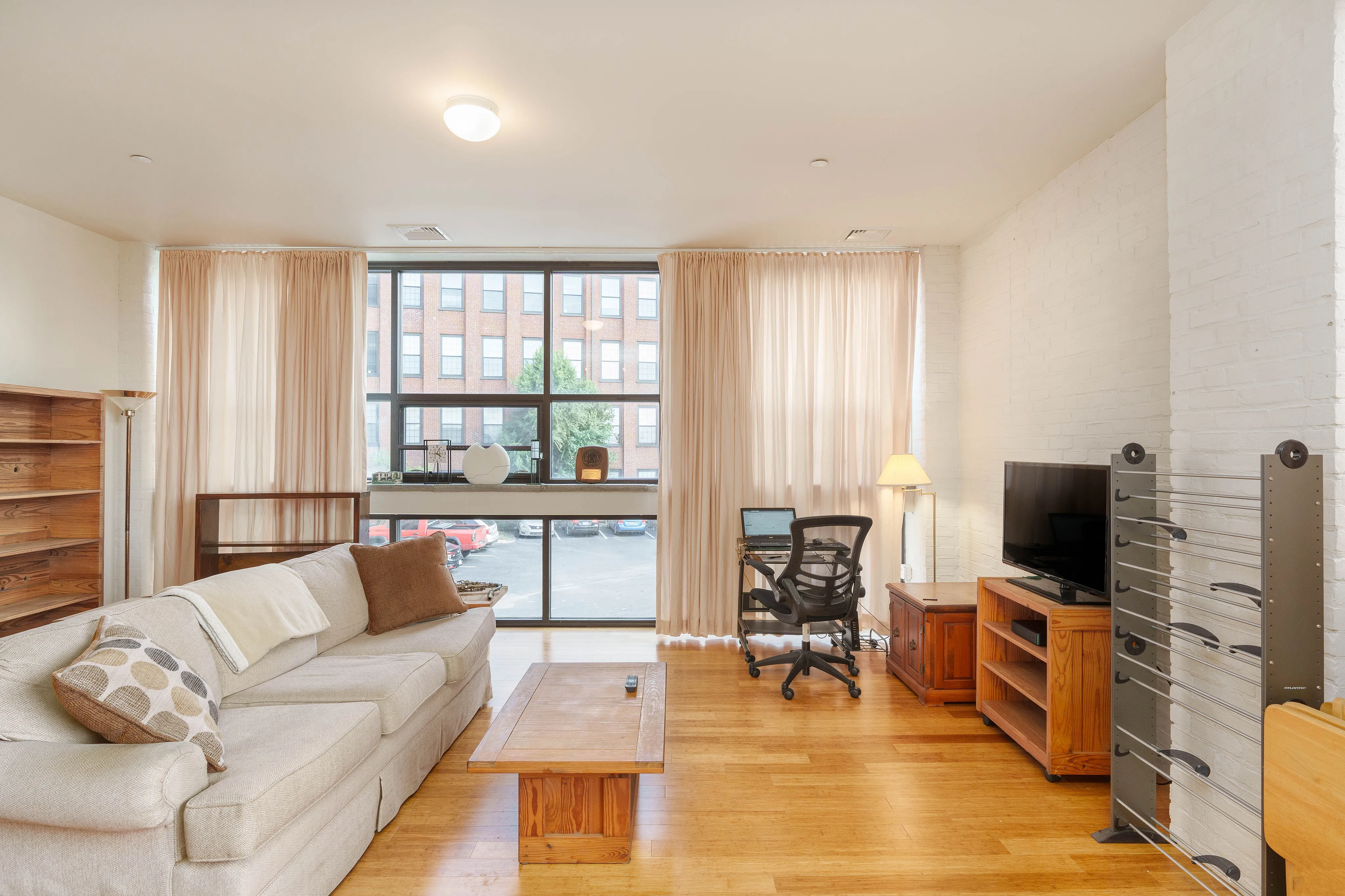Bright and spacious living room with cozy sofa, modern desk setup, large window with natural light, and stylish decor.