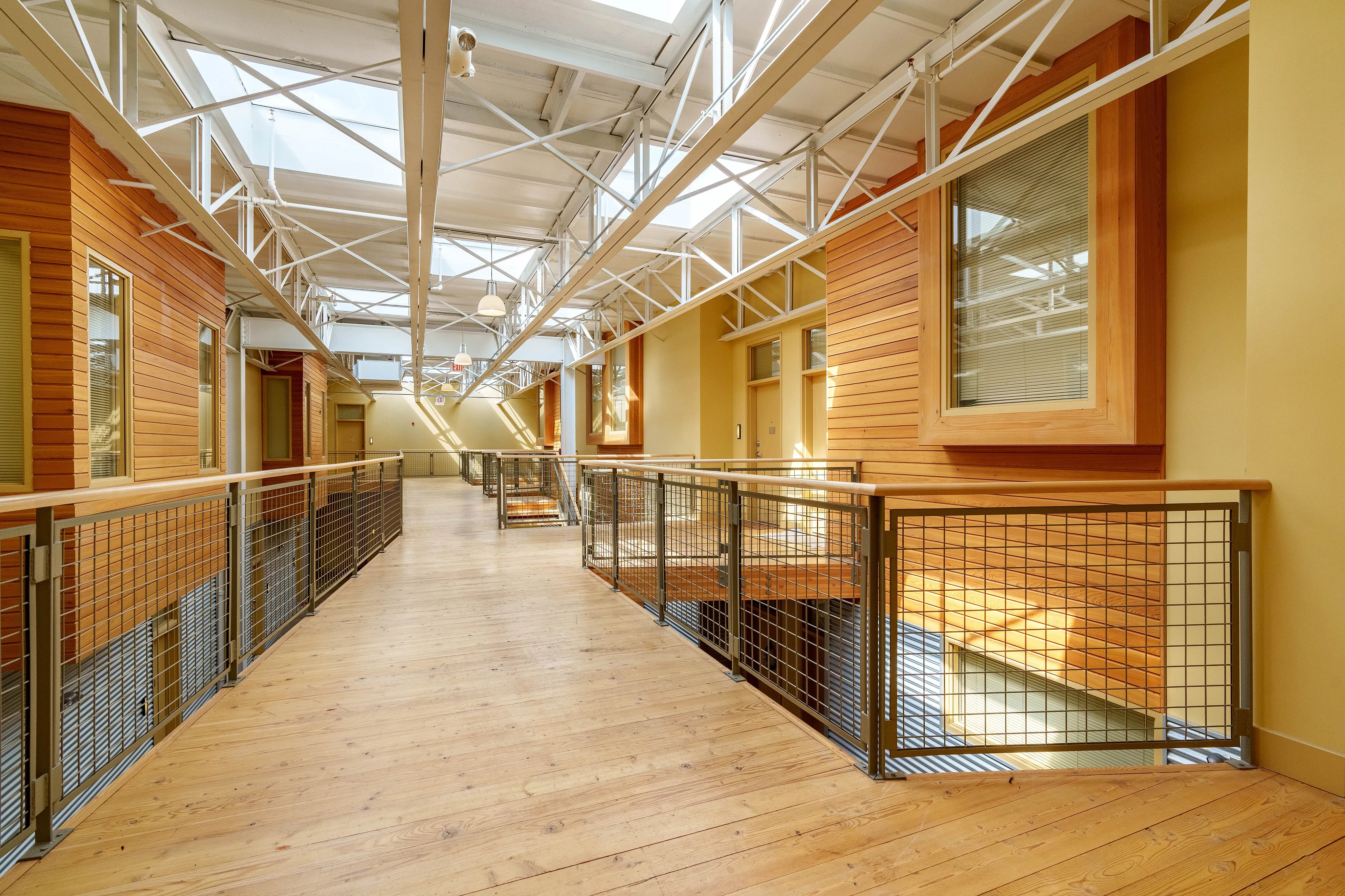 Bright and spacious corridor with wooden accents, featuring large windows and sleek metal railings.