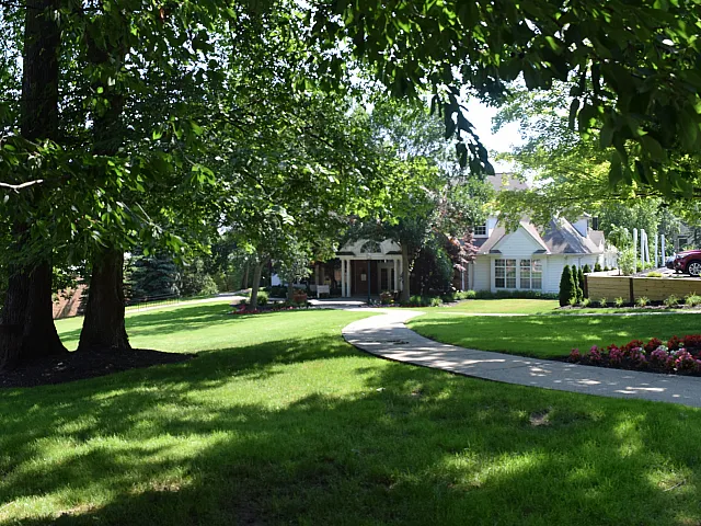 Charming residential path leading to a cozy house surrounded by lush greenery and vibrant flower beds, perfect for tranquil living.