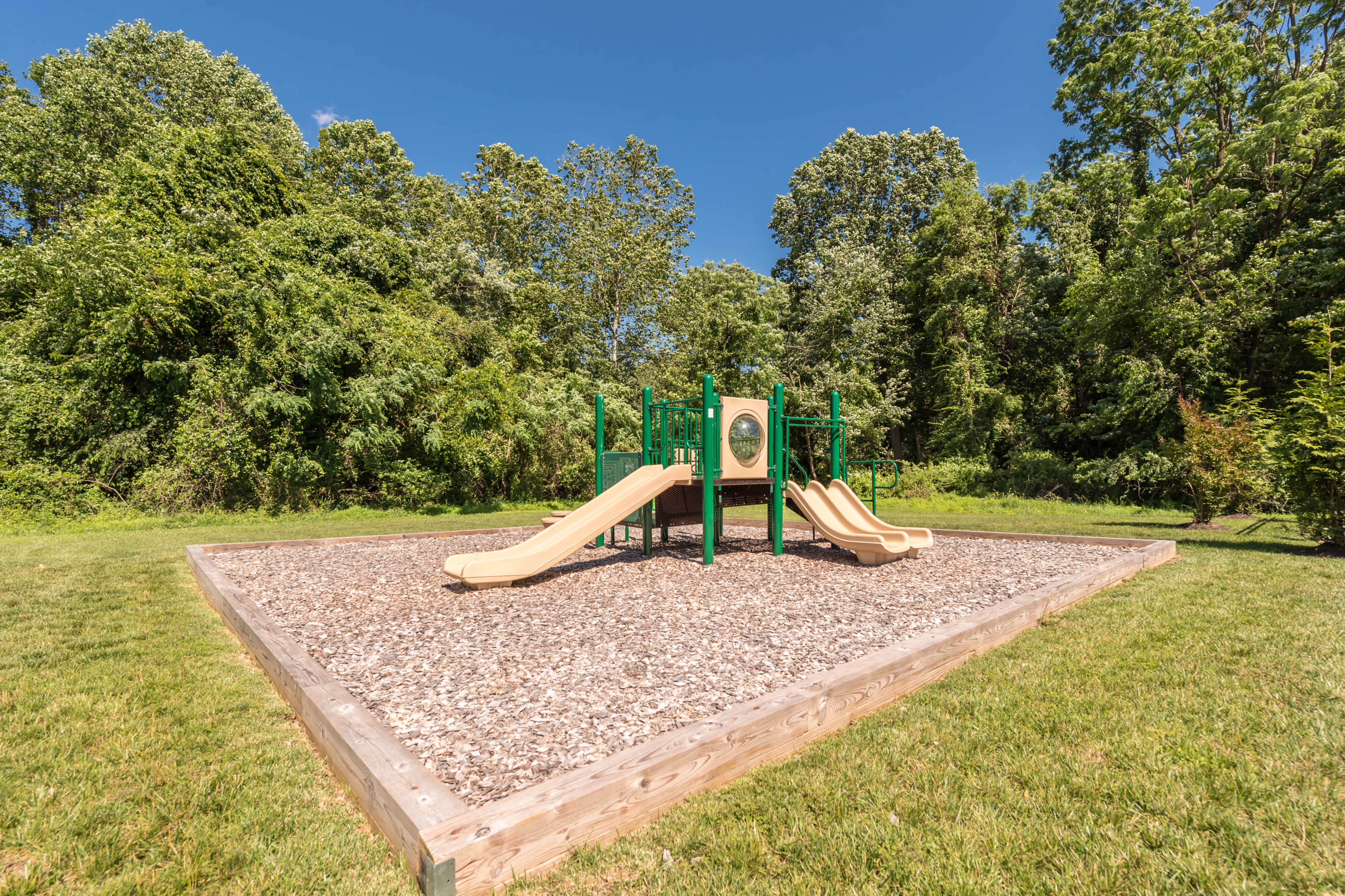 Charming playground with two slides surrounded by lush greenery, perfect for family fun in a serene outdoor setting.