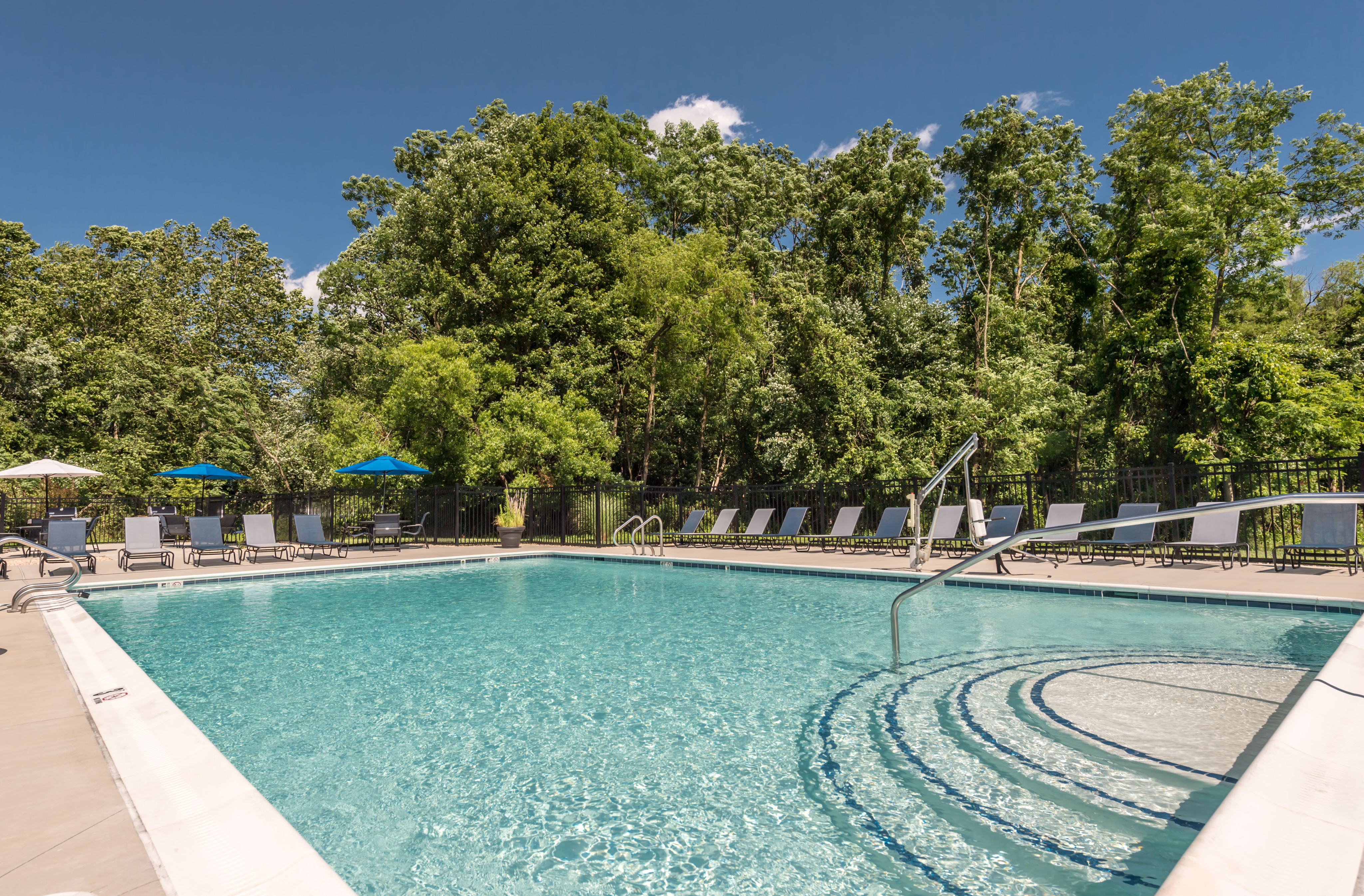 Luxurious outdoor pool area with crystal-clear water, surrounded by sun loungers and vibrant green trees, perfect for relaxation.