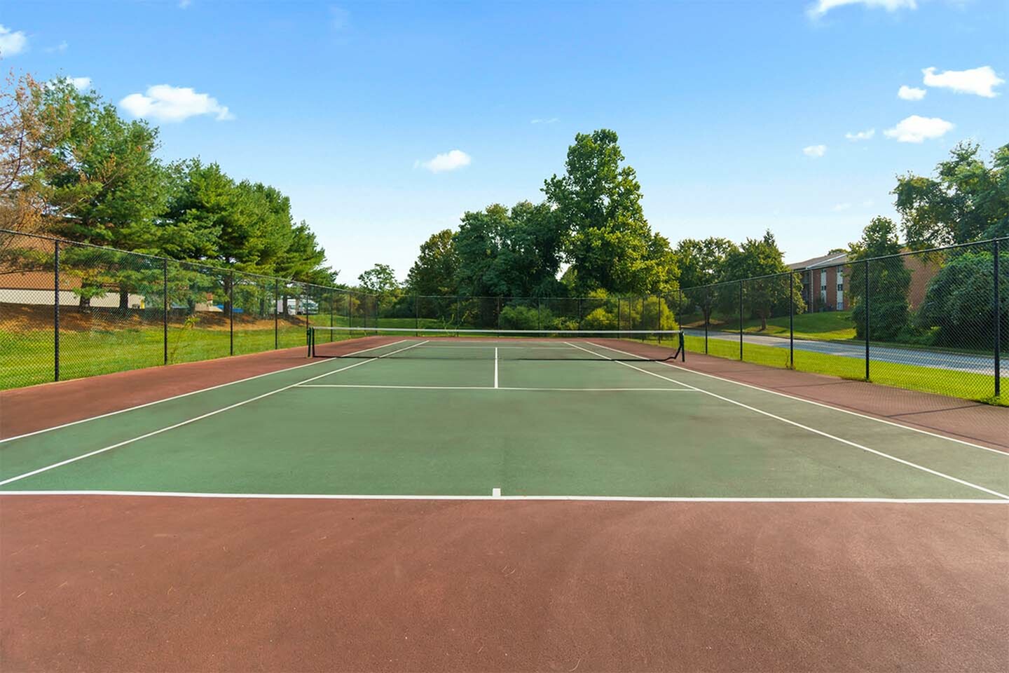 Expansive outdoor tennis court surrounded by lush greenery, perfect for active living and recreation.