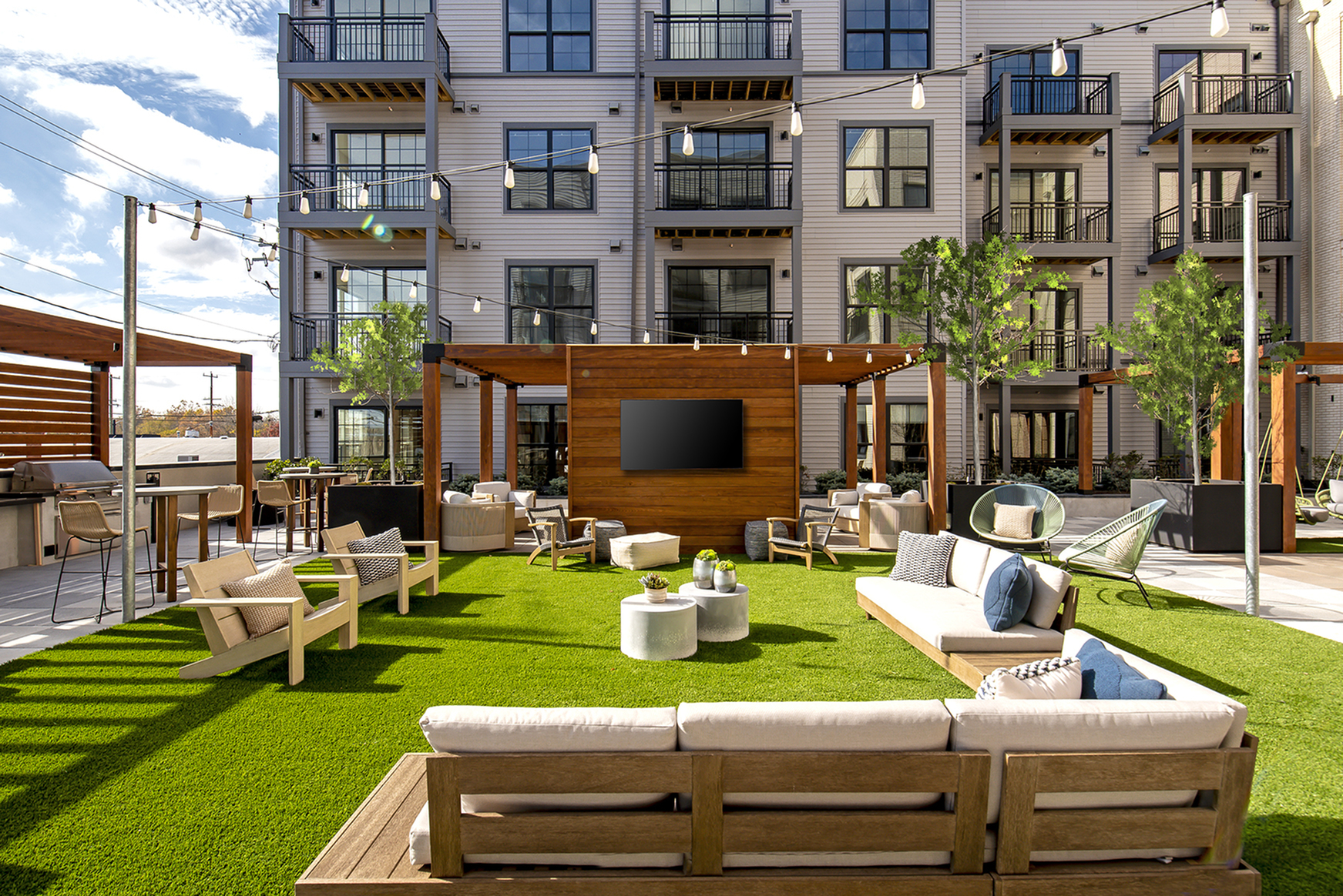 Elegant apartment complex courtyard featuring stylish outdoor furniture, lush green lawn, and charming string lights for a relaxing ambiance.