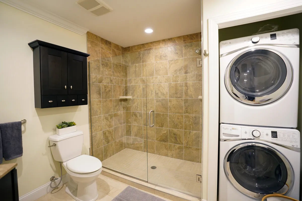 Elegant bathroom with a spacious glass-enclosed shower, stylish wood cabinetry, and an in-unit washer and dryer for added convenience.