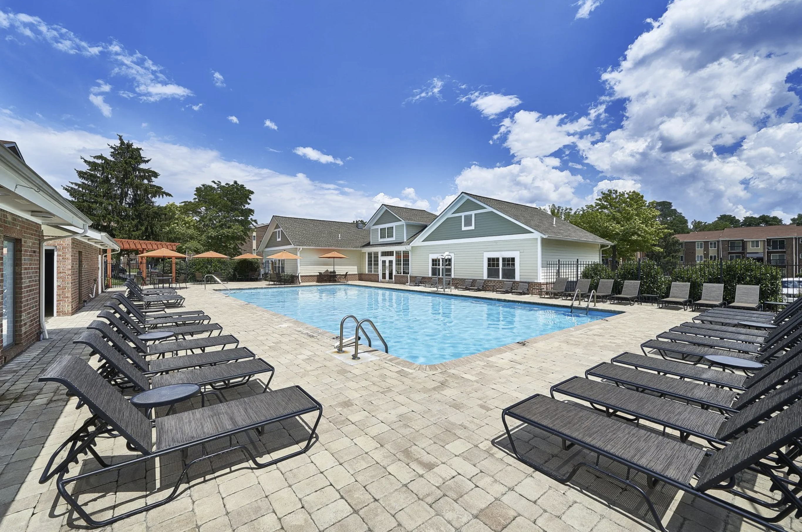 Inviting outdoor pool area with comfortable lounge chairs, surrounded by lush greenery and scenic architecture under a bright blue sky.