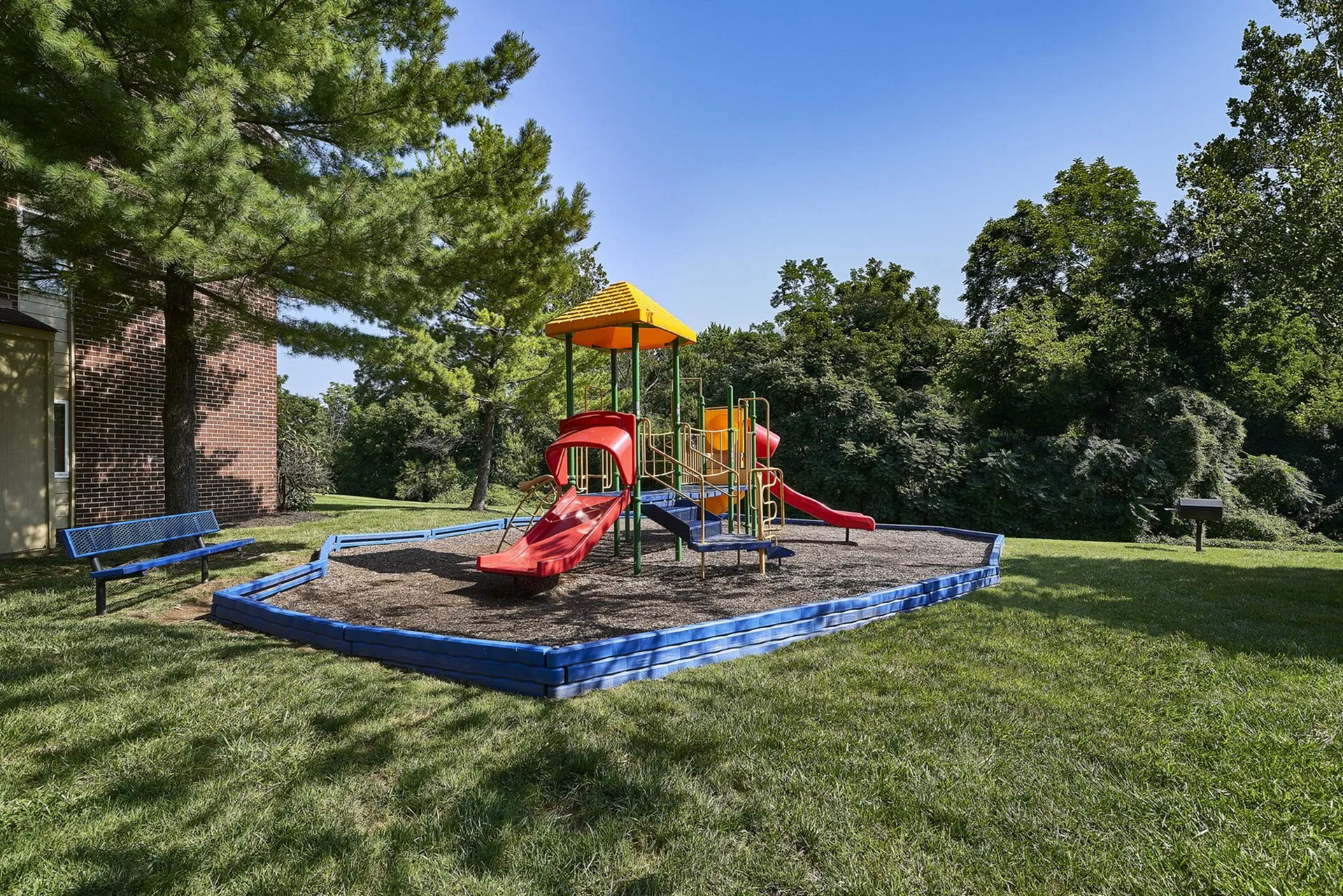 Vibrant playground with bright slides and climbing structures, surrounded by lush trees and well-maintained grass, ideal family-friendly outdoor space.