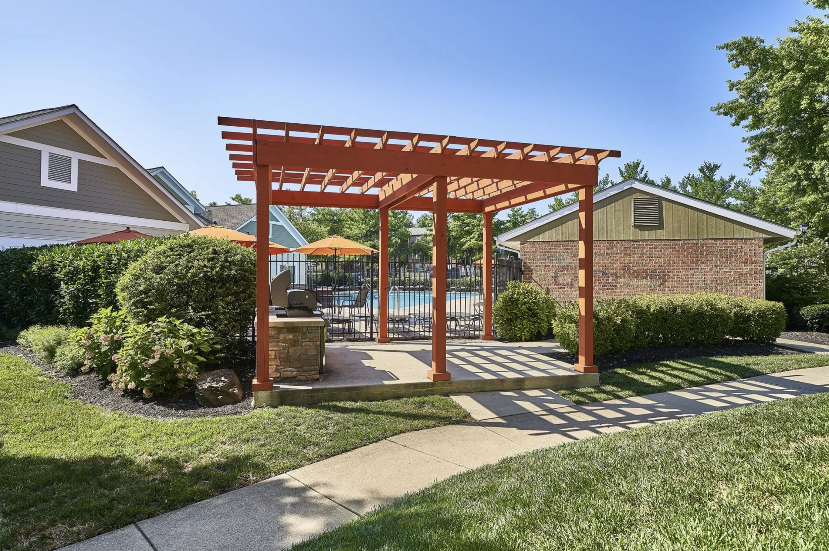 Charming outdoor area featuring a wooden pergola with lush greenery, poolside view, and tranquil garden setting.