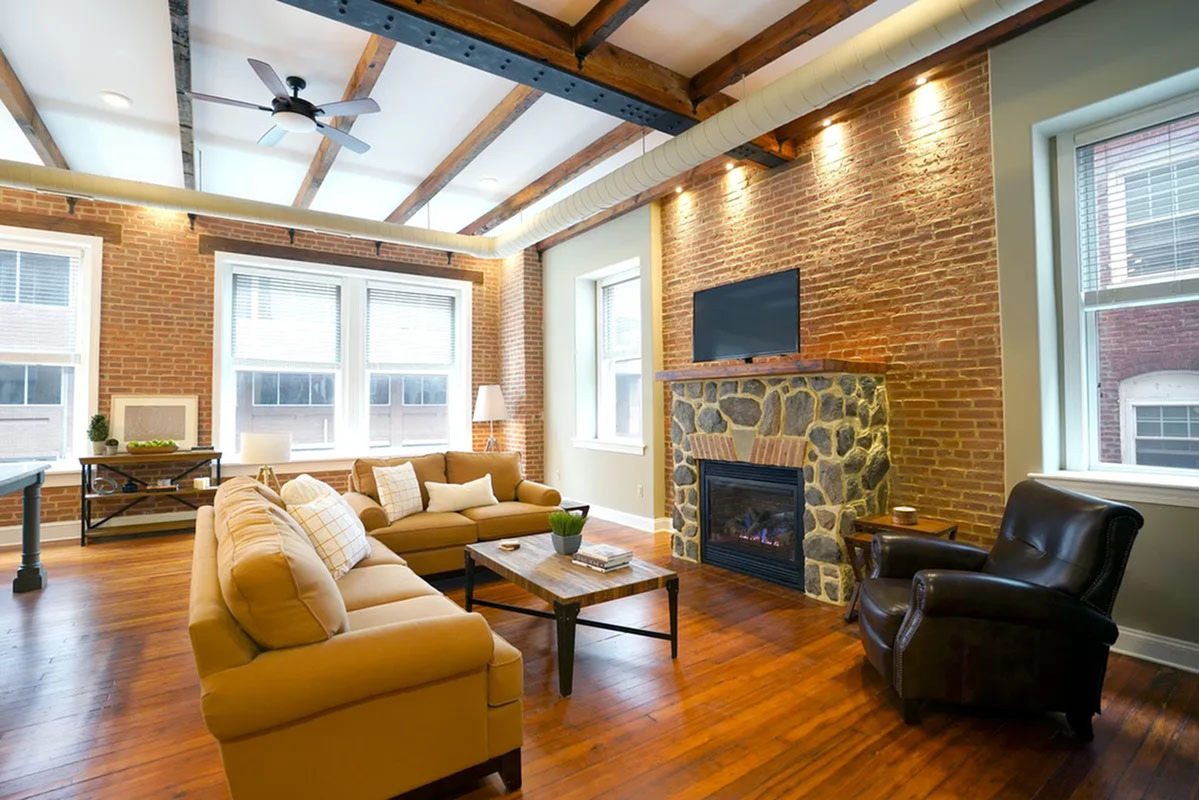 Chic urban living room with exposed brick walls, cozy sofas, stone fireplace, and wood-beamed ceiling.