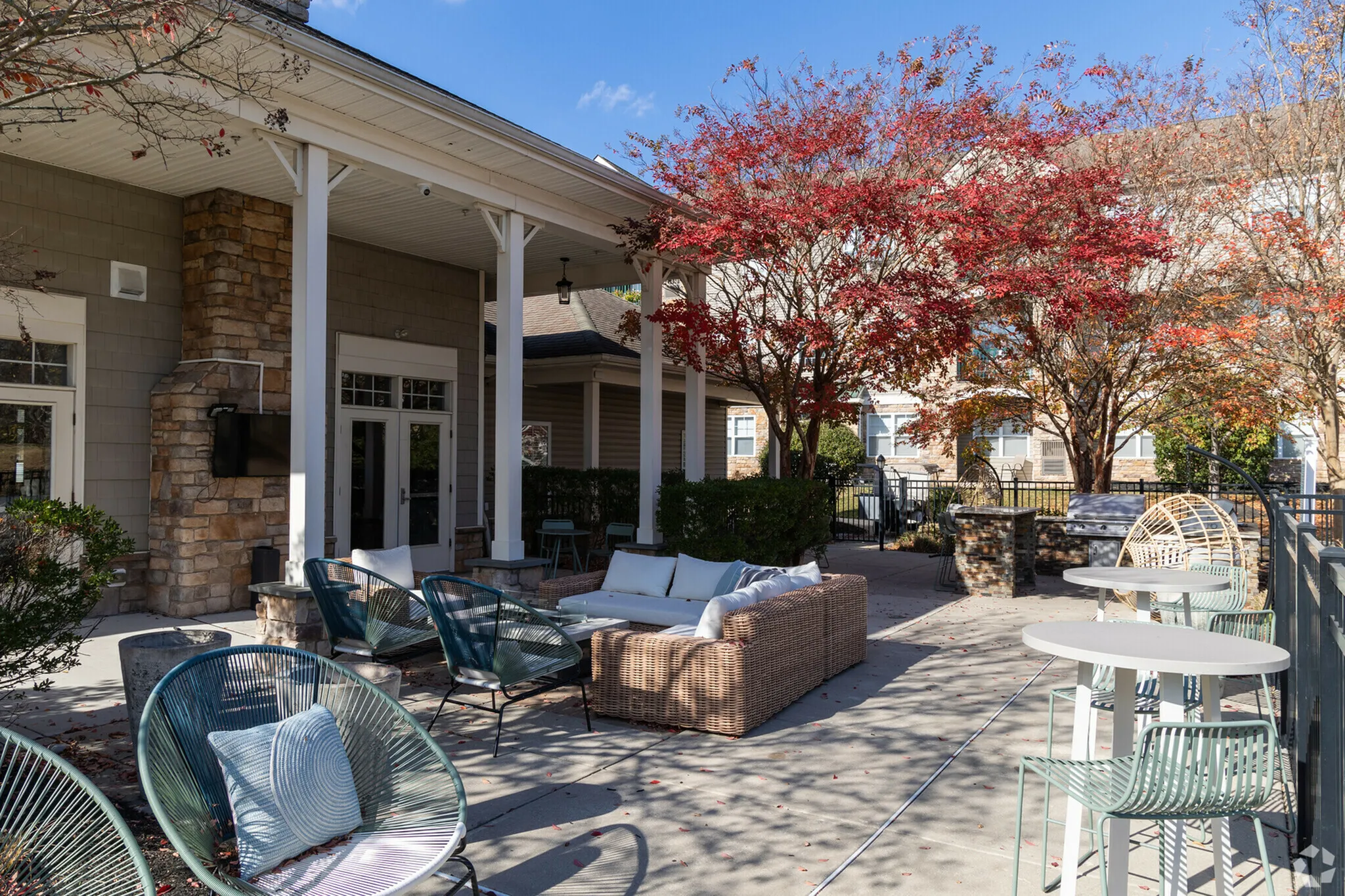 Charming outdoor patio with cozy seating, modern tables, and vibrant autumn trees, perfect for relaxation and gatherings.