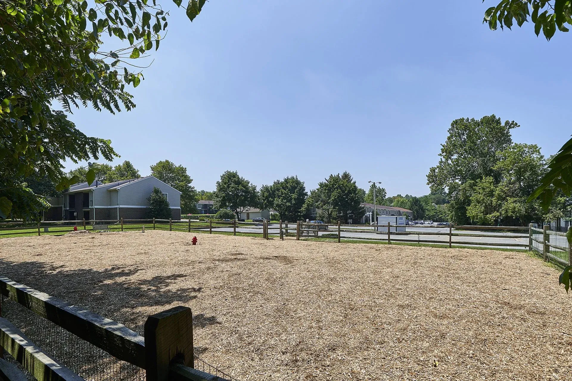 Bright and inviting outdoor space featuring a fenced sandy area perfect for activities, set against a backdrop of lush trees and charming homes.