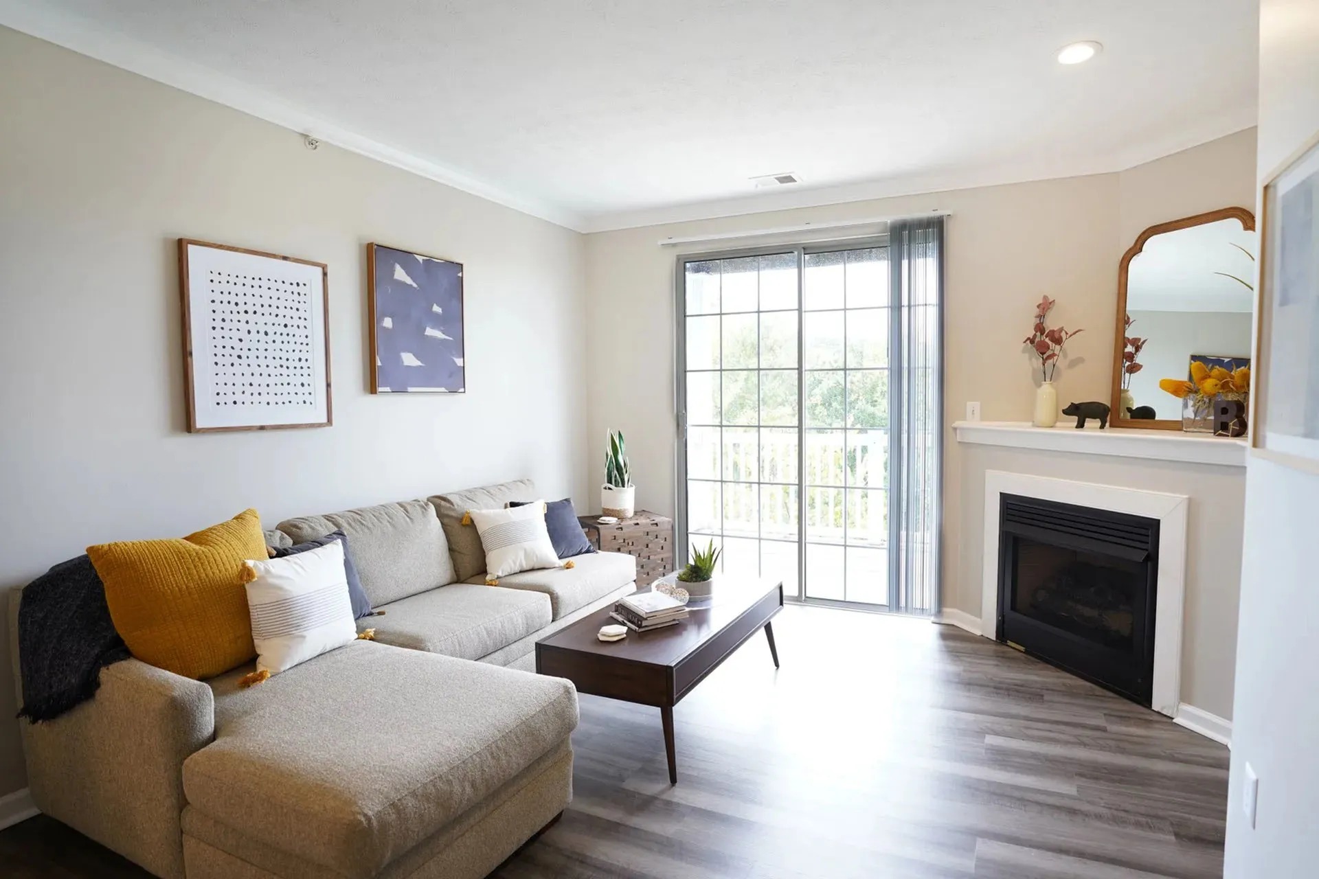 Bright and inviting living room with a cozy gray sectional, stylish artwork, and a modern fireplace, accentuated by natural light from large sliding glass doors.