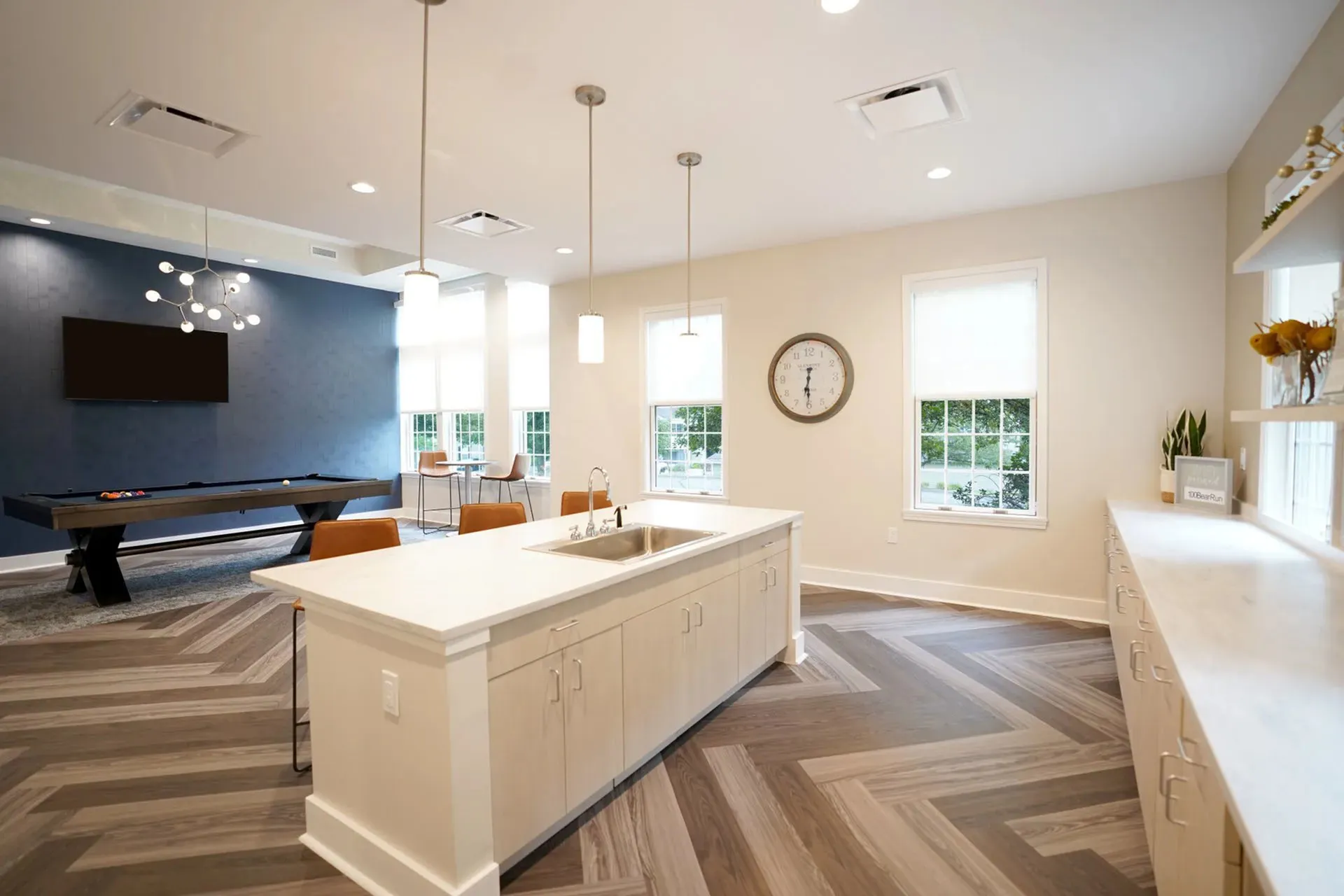 Modern open-plan kitchen and living area with sleek cabinetry, stylish lighting, and a pool table against a chic blue accent wall.