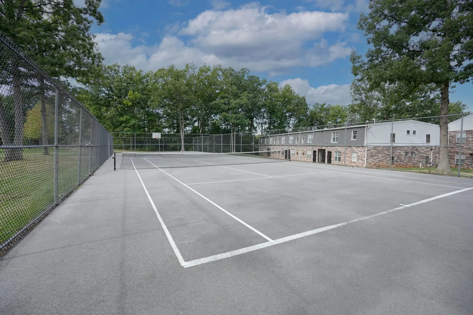 Inviting apartment complex with a well-maintained tennis court surrounded by lush greenery and beautiful skies.
