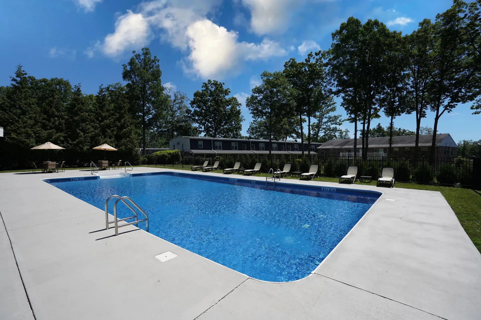 Inviting outdoor swimming pool surrounded by lush greenery and lounge chairs under a clear blue sky.