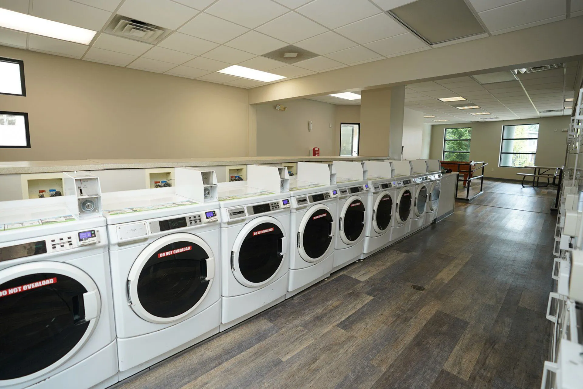 Modern apartment laundry room with multiple washers, bright lighting, and seating area for residents.
