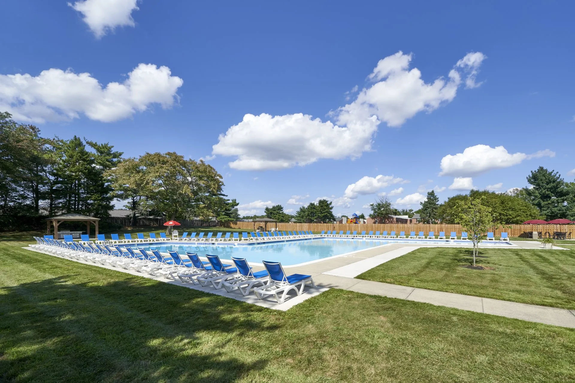 Serene outdoor swimming pool surrounded by lush greenery and bright blue lounge chairs under a clear sky.