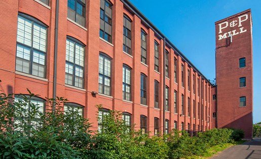 Charming loft apartment in a historic red brick mill with large windows and lush greenery, blending industrial heritage with modern living.