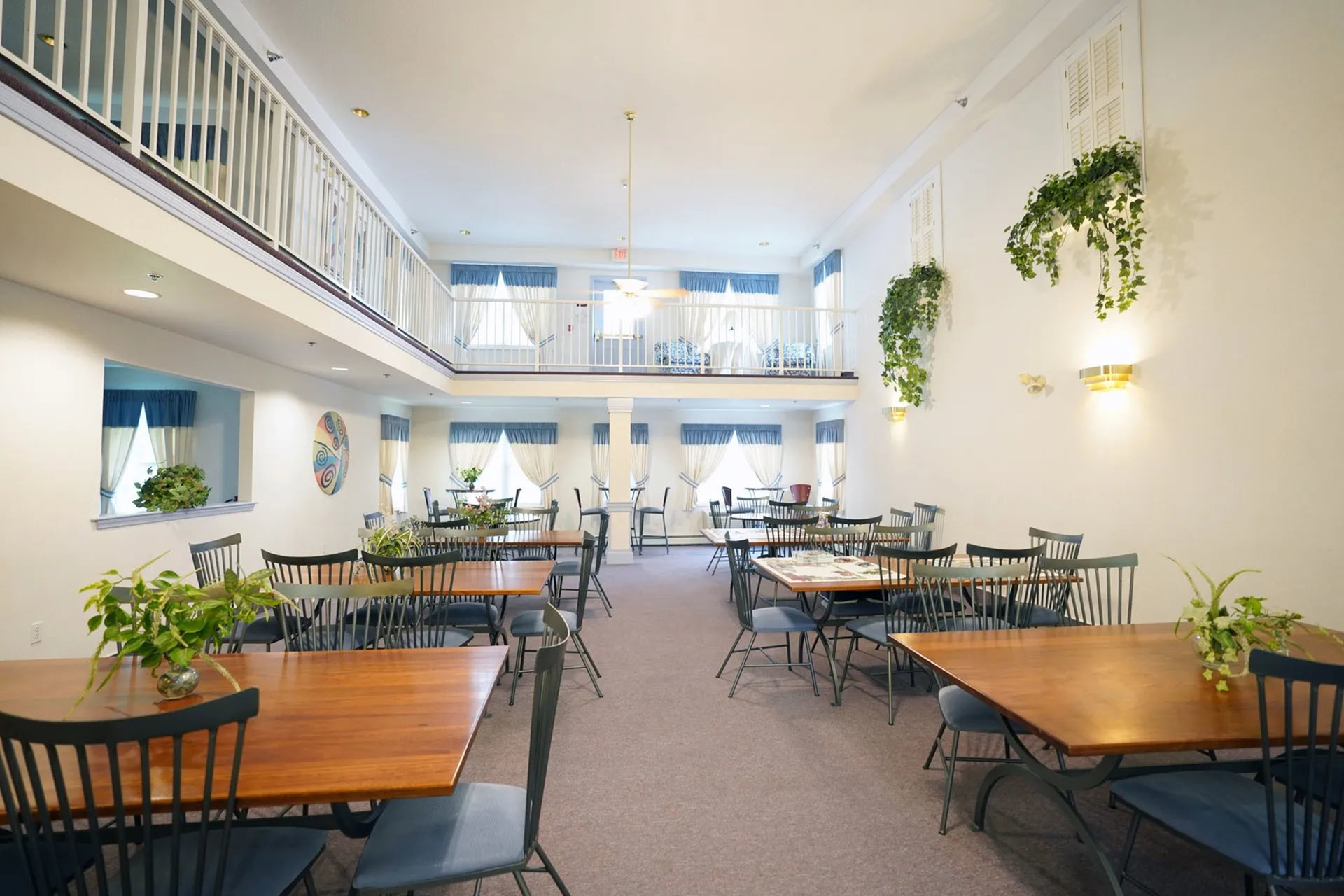 Bright and welcoming dining area with elegant wooden tables, lush greenery, and a charming second-floor balcony view.