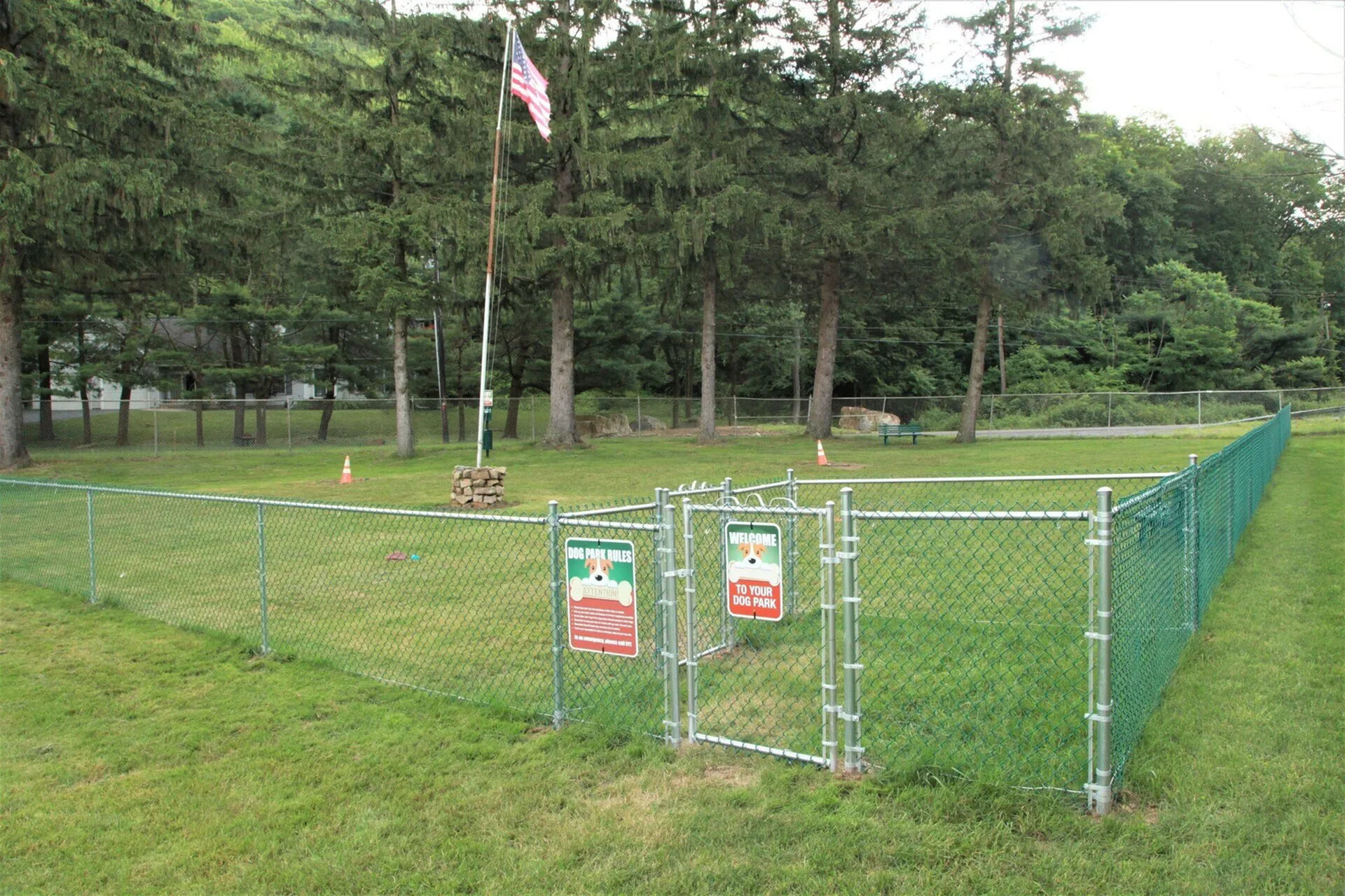 Inviting fenced dog park surrounded by lush greenery, featuring a welcoming entrance and a flagpole, perfect for pet owners seeking a serene outdoor retreat.