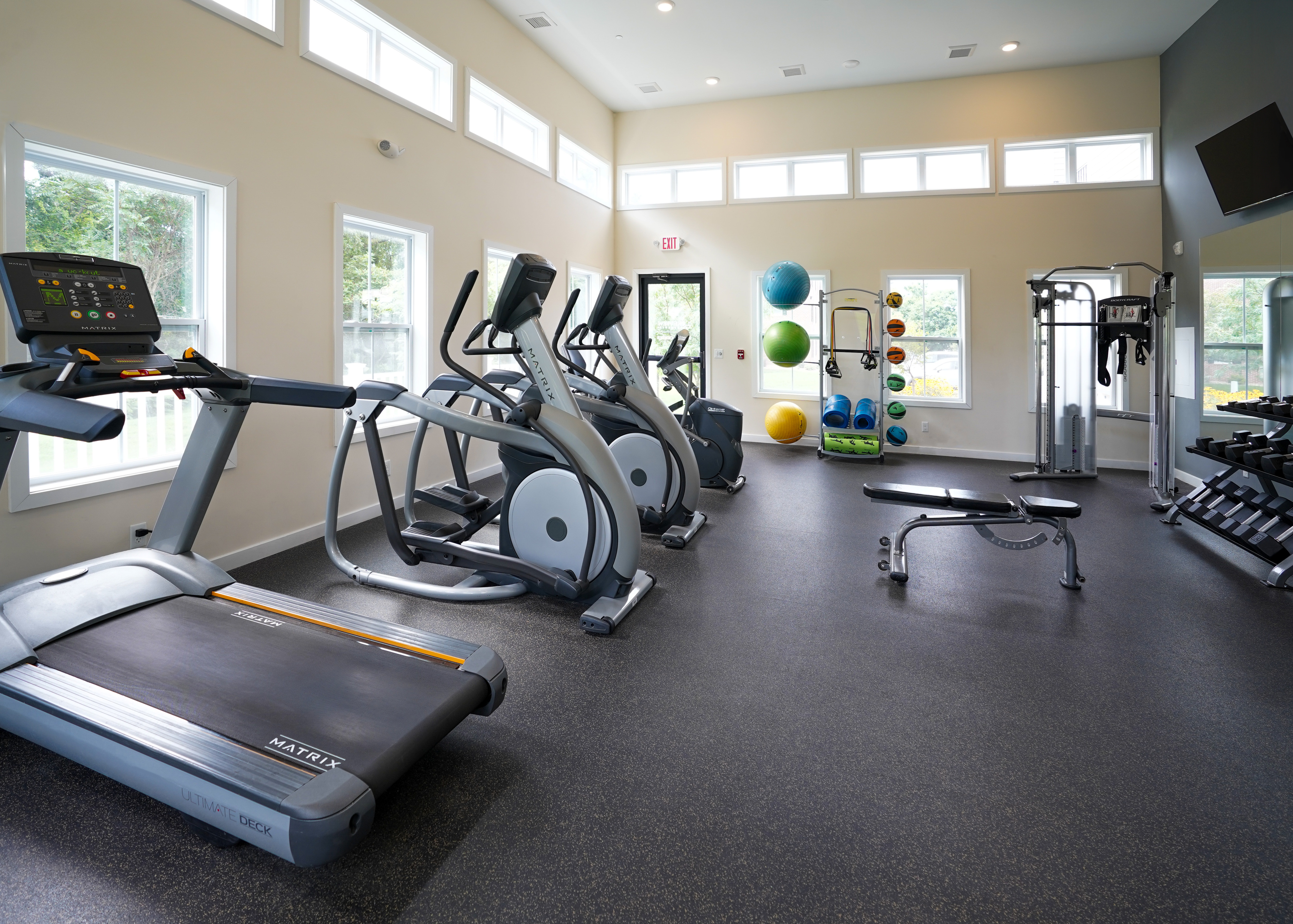 Bright and modern fitness center featuring state-of-the-art treadmills, ellipticals, and a range of exercise equipment with ample natural light.