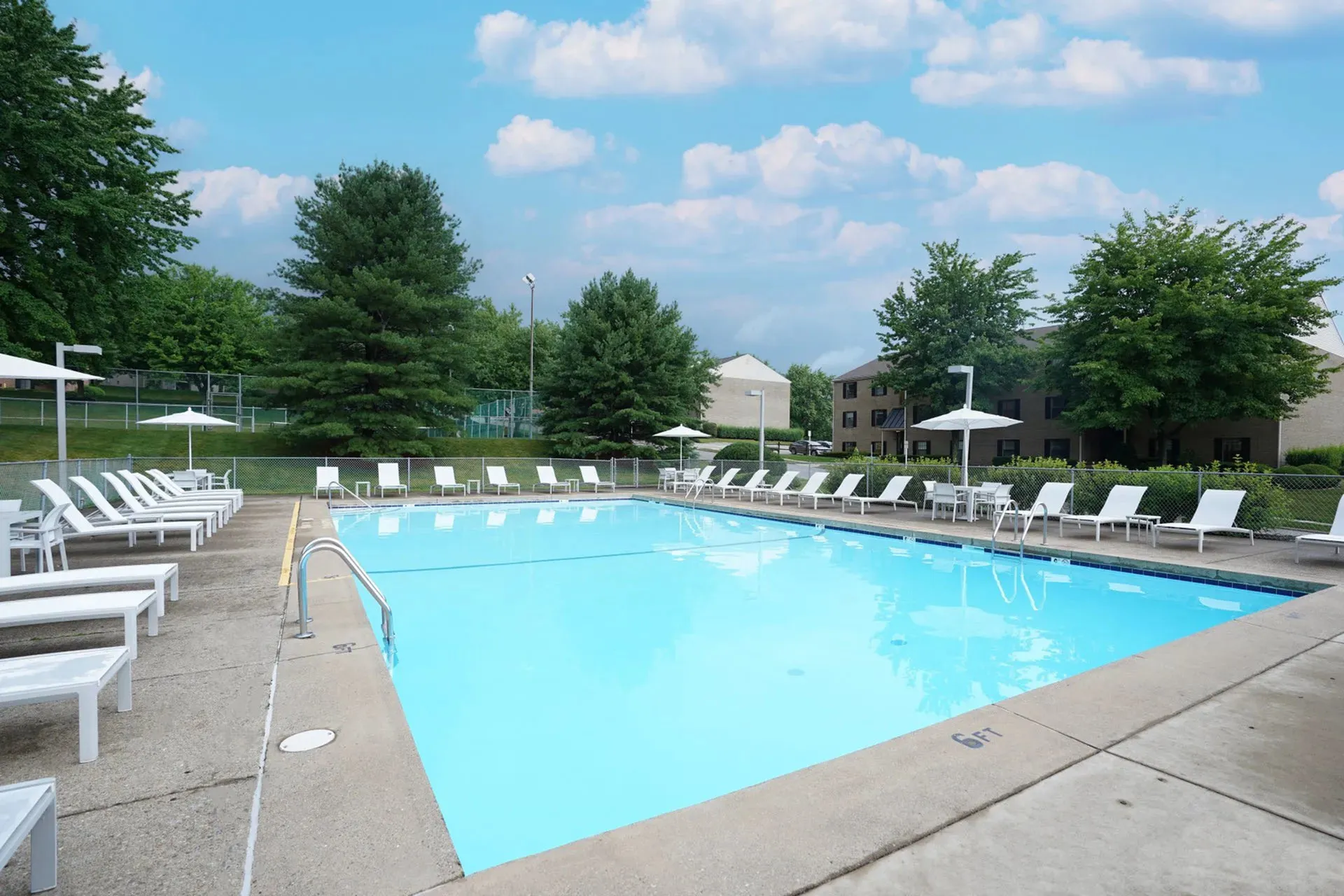 Inviting outdoor swimming pool with sun loungers and umbrellas set against lush greenery and clear skies.