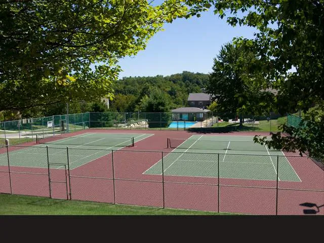 Vibrant apartment community tennis courts surrounded by lush greenery and a view of the inviting swimming pool.