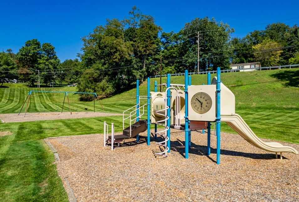 Inviting playground surrounded by lush green landscape, featuring slides and swings under a clear blue sky.