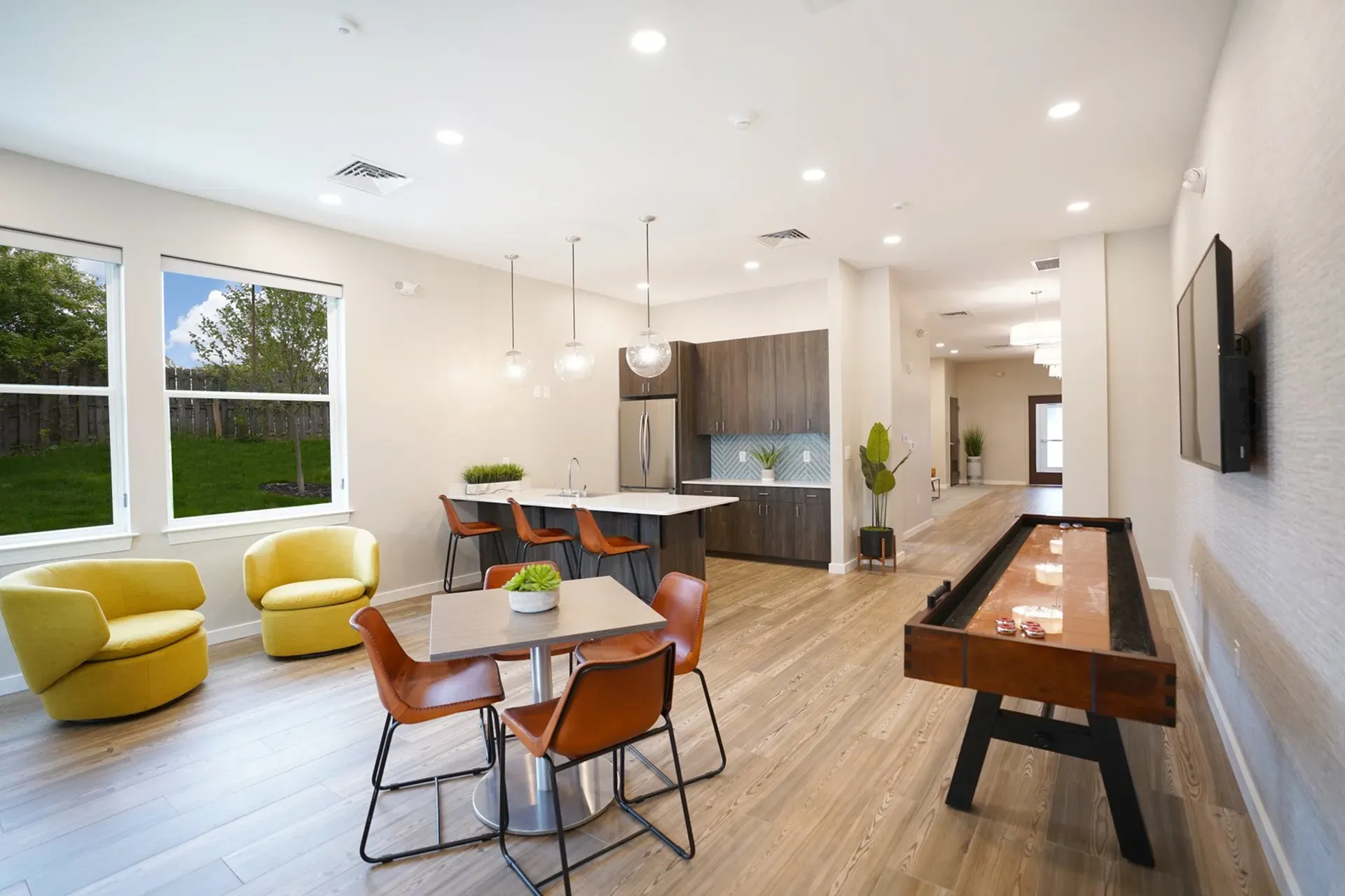 Modern apartment interior featuring an open-concept kitchen with sleek cabinetry and a stylish dining area with leather chairs, accented by large windows and vibrant yellow armchairs.