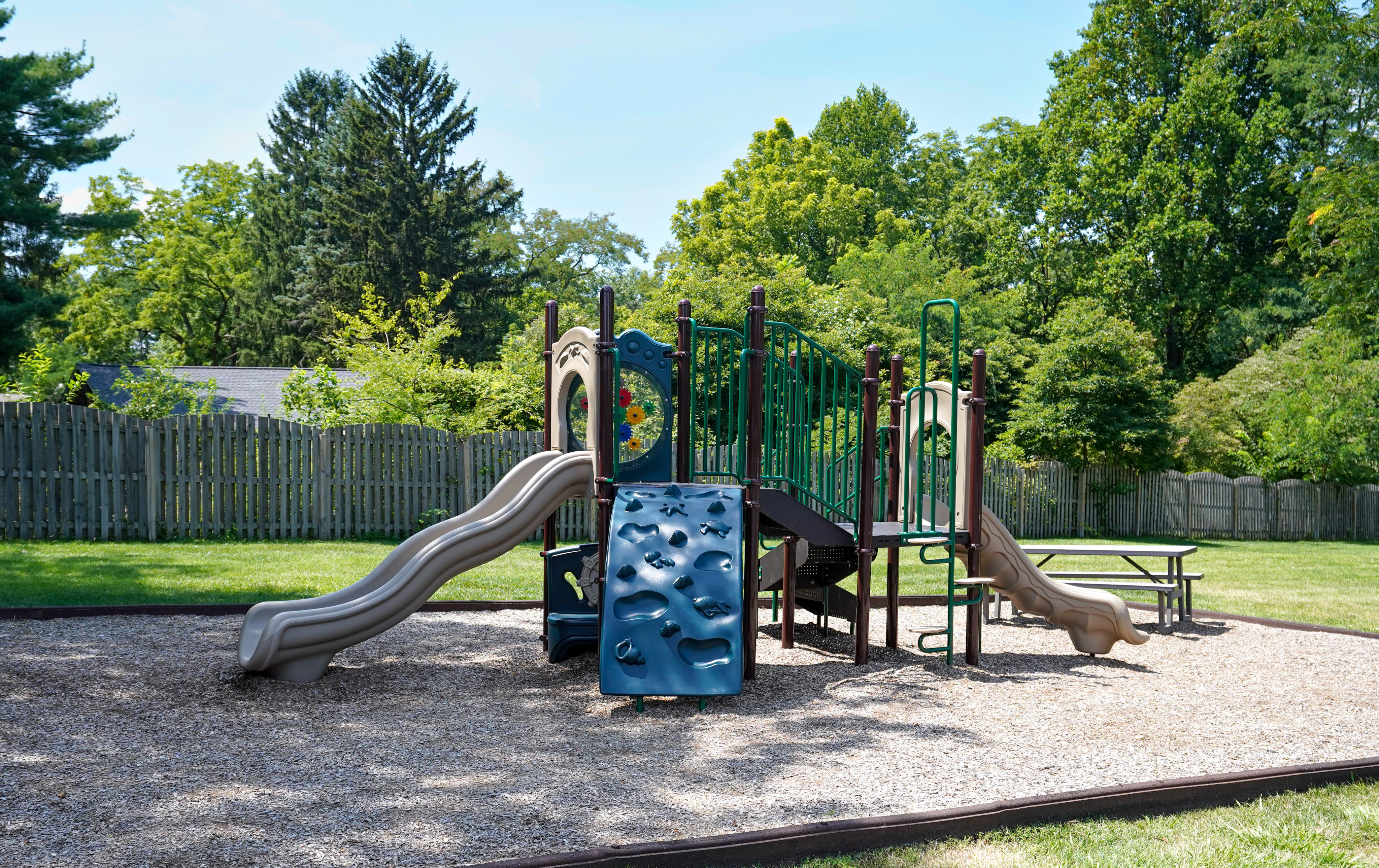 Inviting playground in a lush green setting, showcasing slides, climbing wall, and picnic area, perfect for family fun and outdoor enjoyment.