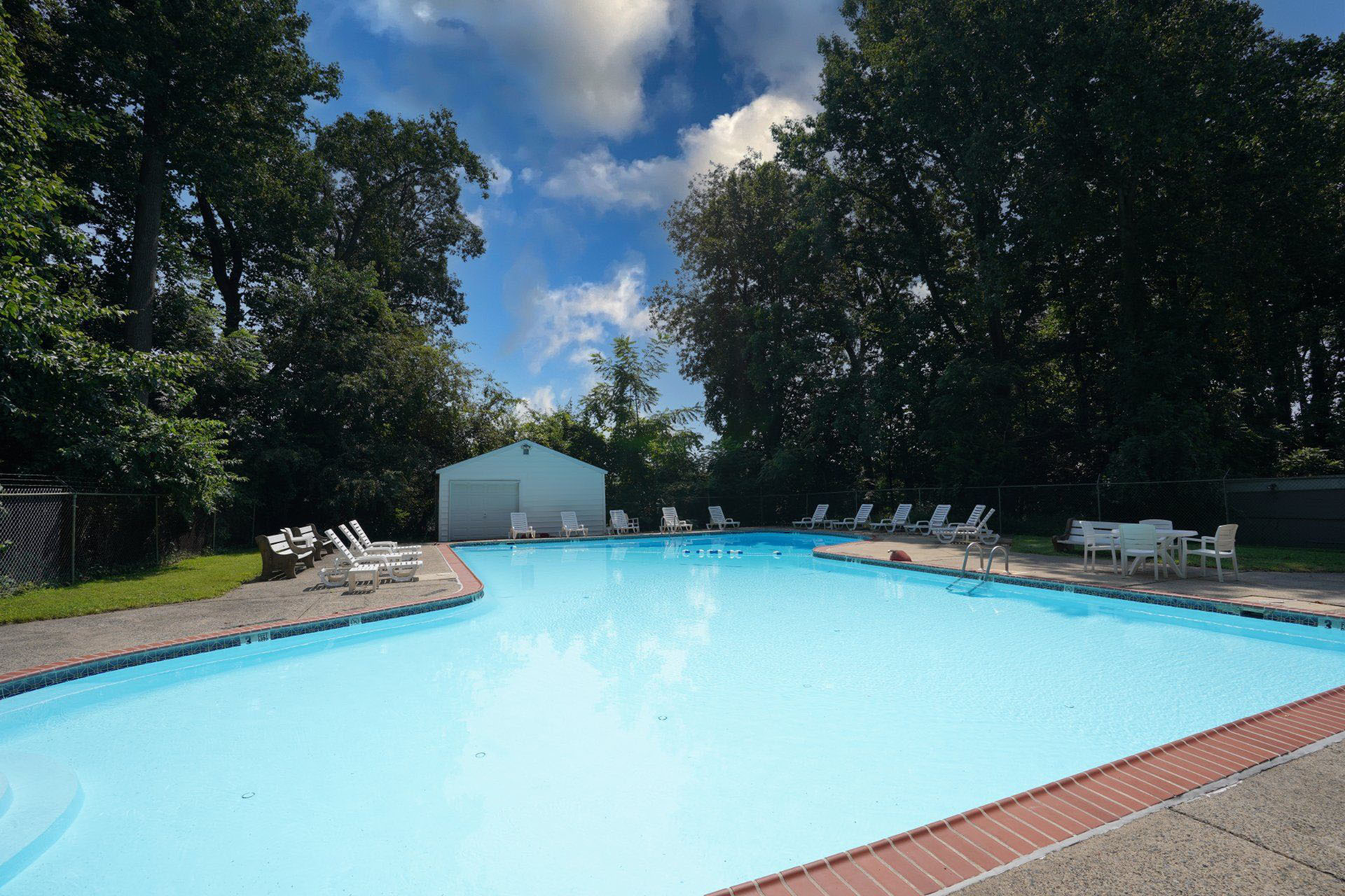 Inviting outdoor pool area surrounded by lush trees, featuring sun loungers and a serene atmosphere.