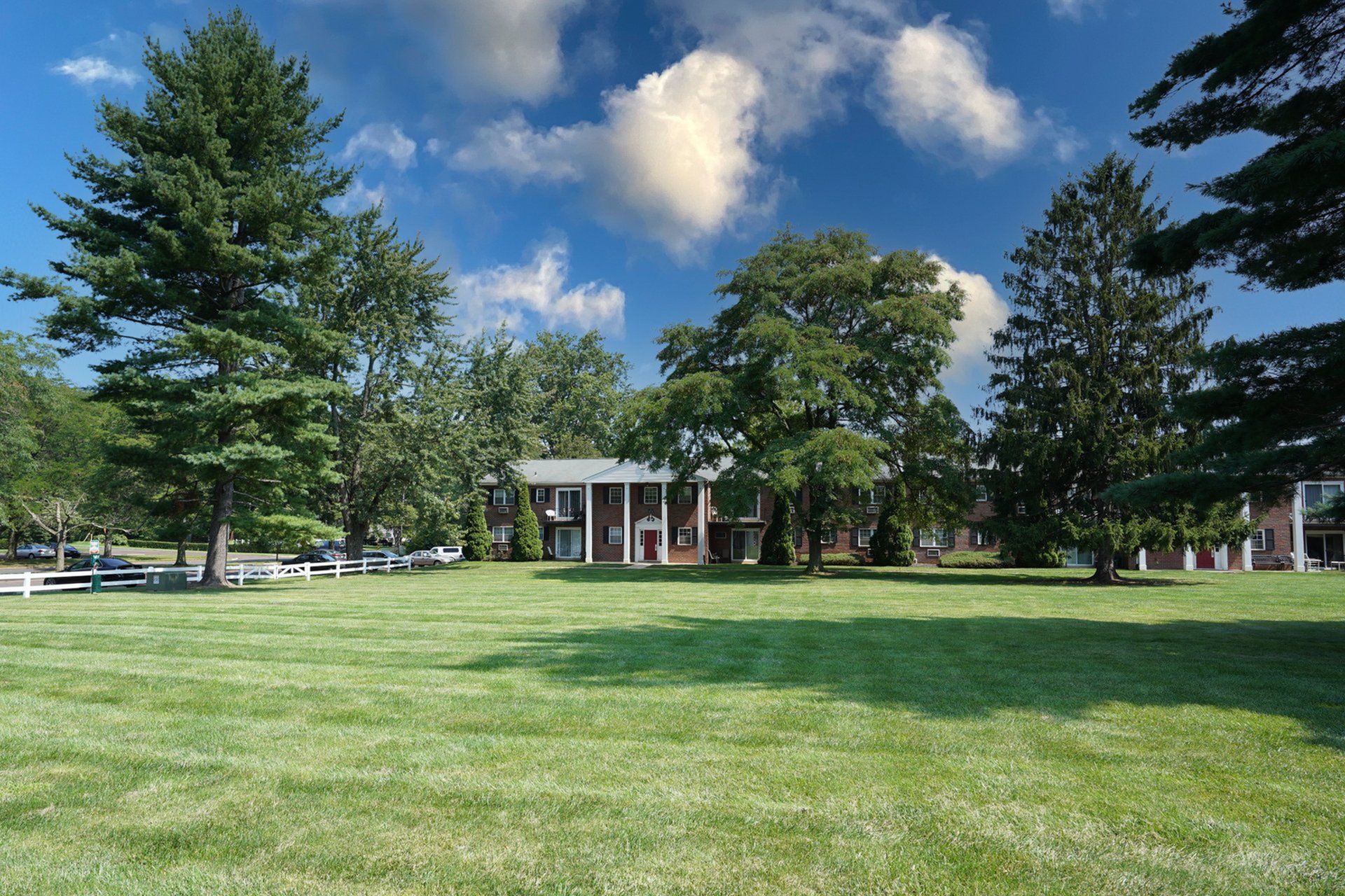 Charming apartment complex nestled amidst lush greenery and tall trees under a vibrant blue sky.