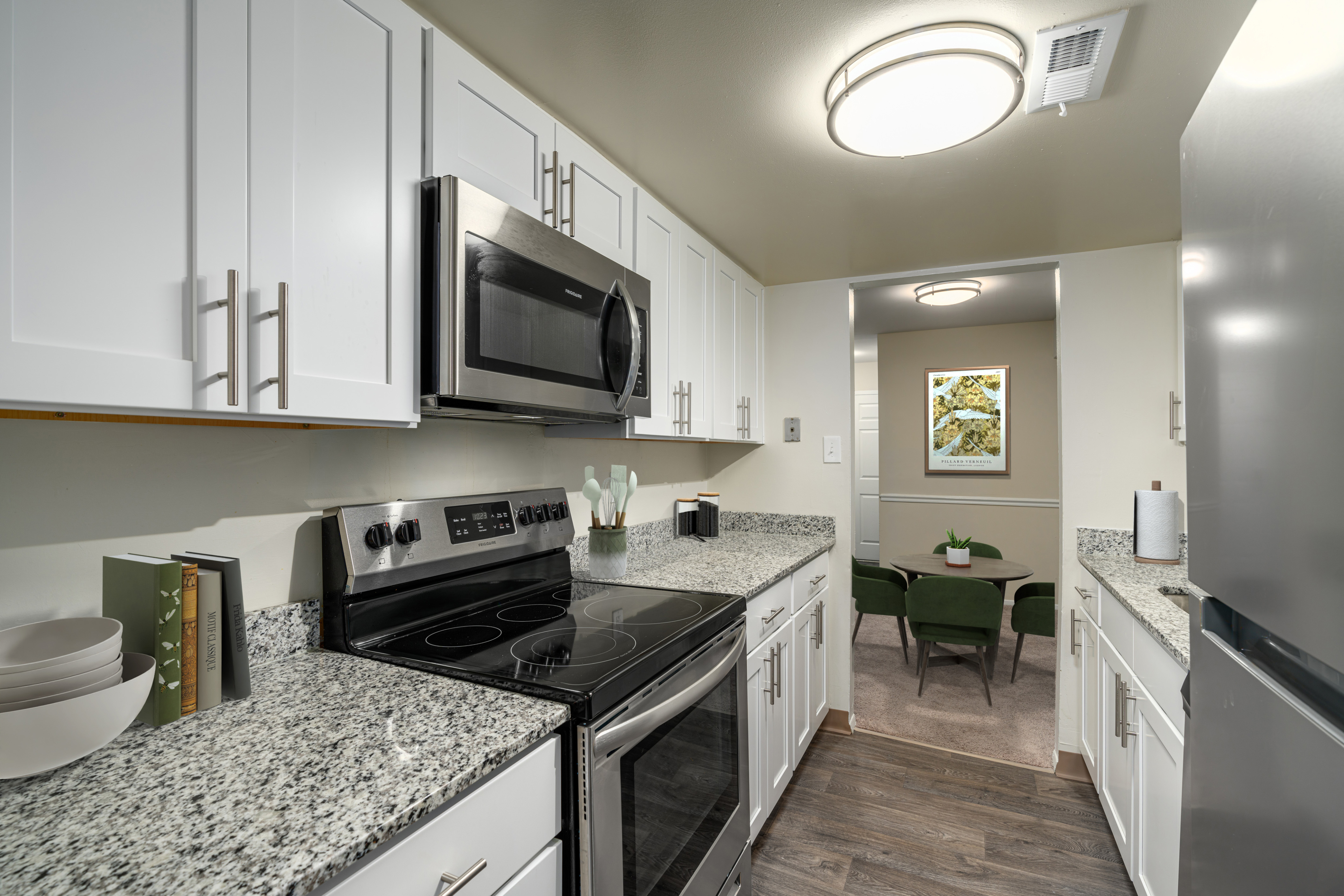 Modern kitchen with sleek white cabinetry, stainless steel appliances, granite countertops, and a view into an inviting dining area with stylish green chairs.