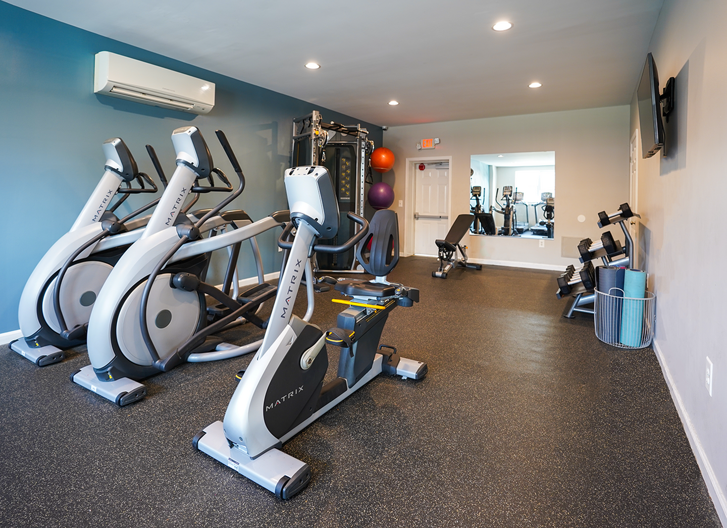Modern gym facility with high-end exercise equipment, including ellipticals, weights, and a workout bench in a spacious, brightly lit room.