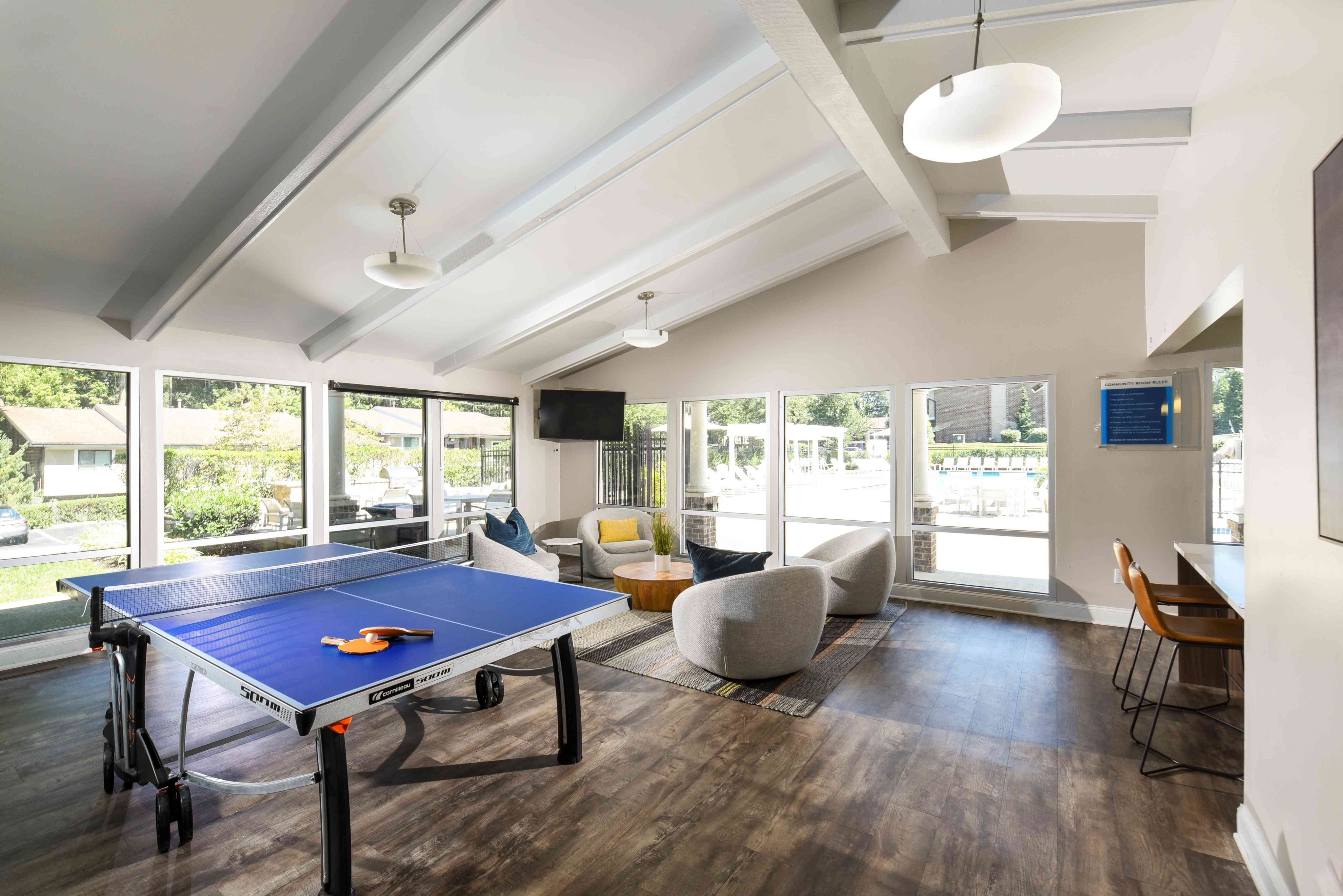 Inviting recreational area with a stylish ping pong table, cozy seating, and large windows offering scenic views.